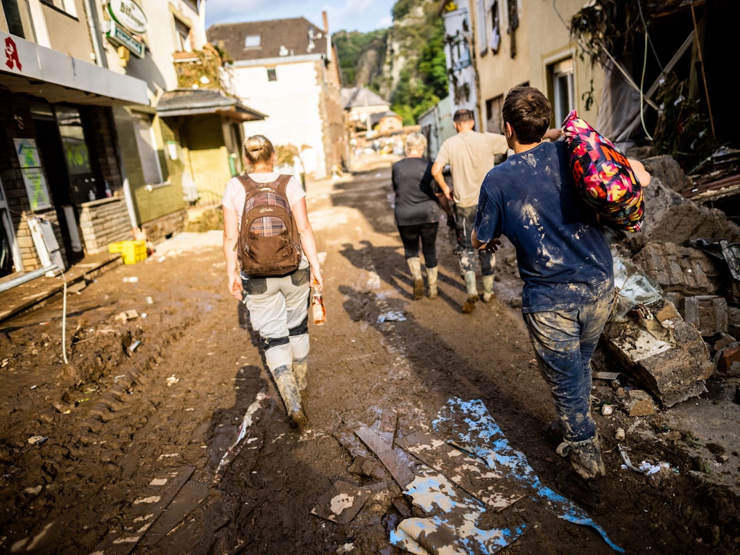 Mit Schlamm verschmierte Helfer und Helferinnen gehen durch Altenahr nach Hause.