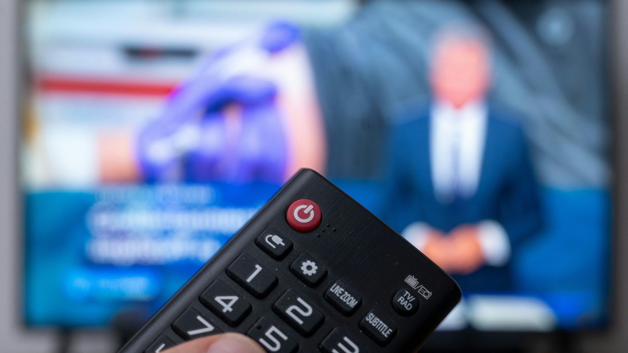 Ein Mann hält eine Fernbedienung vor einen Fernseher, auf dem die Tagesschau läuft.