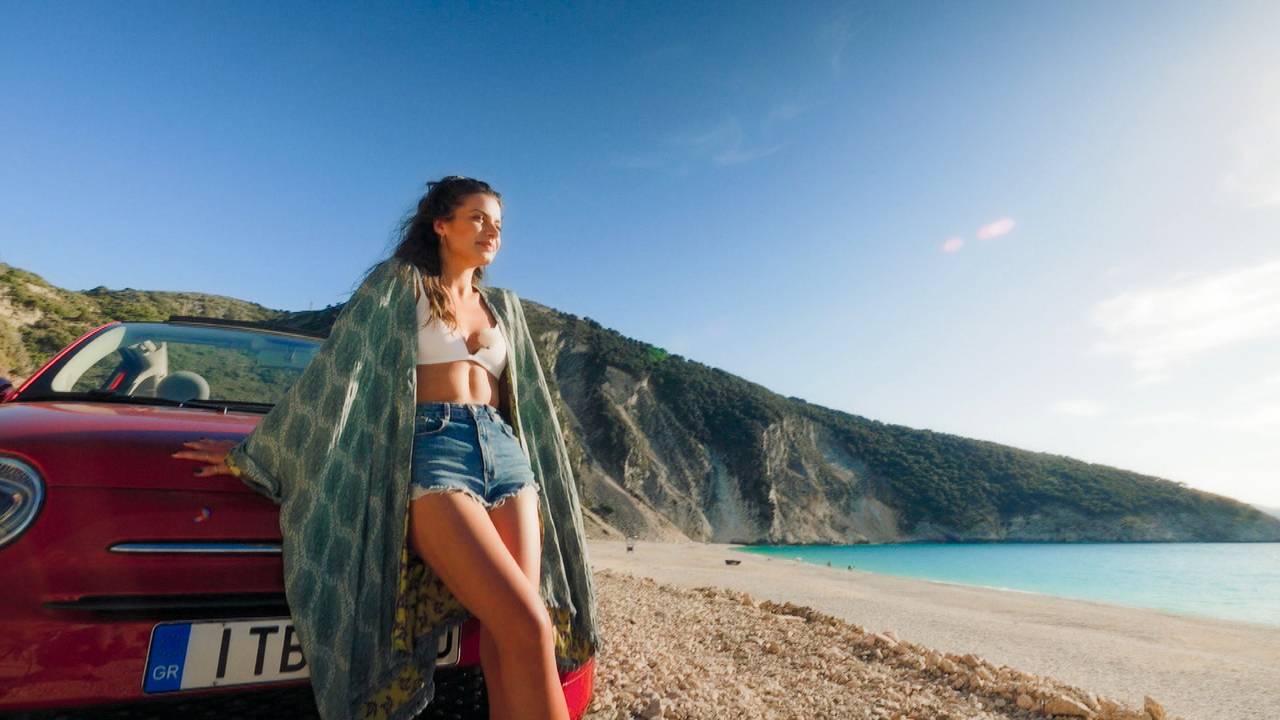 Bachelorette Maxime Herbord lehnt sich an ein Auto am Strand.
