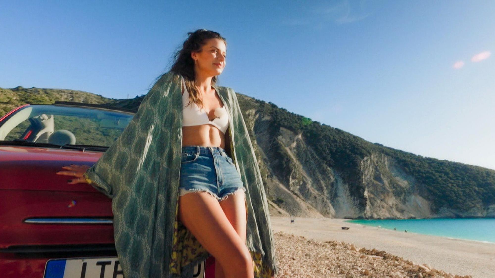 Bachelorette Maxime Herbord lehnt sich an ein Auto am Strand.