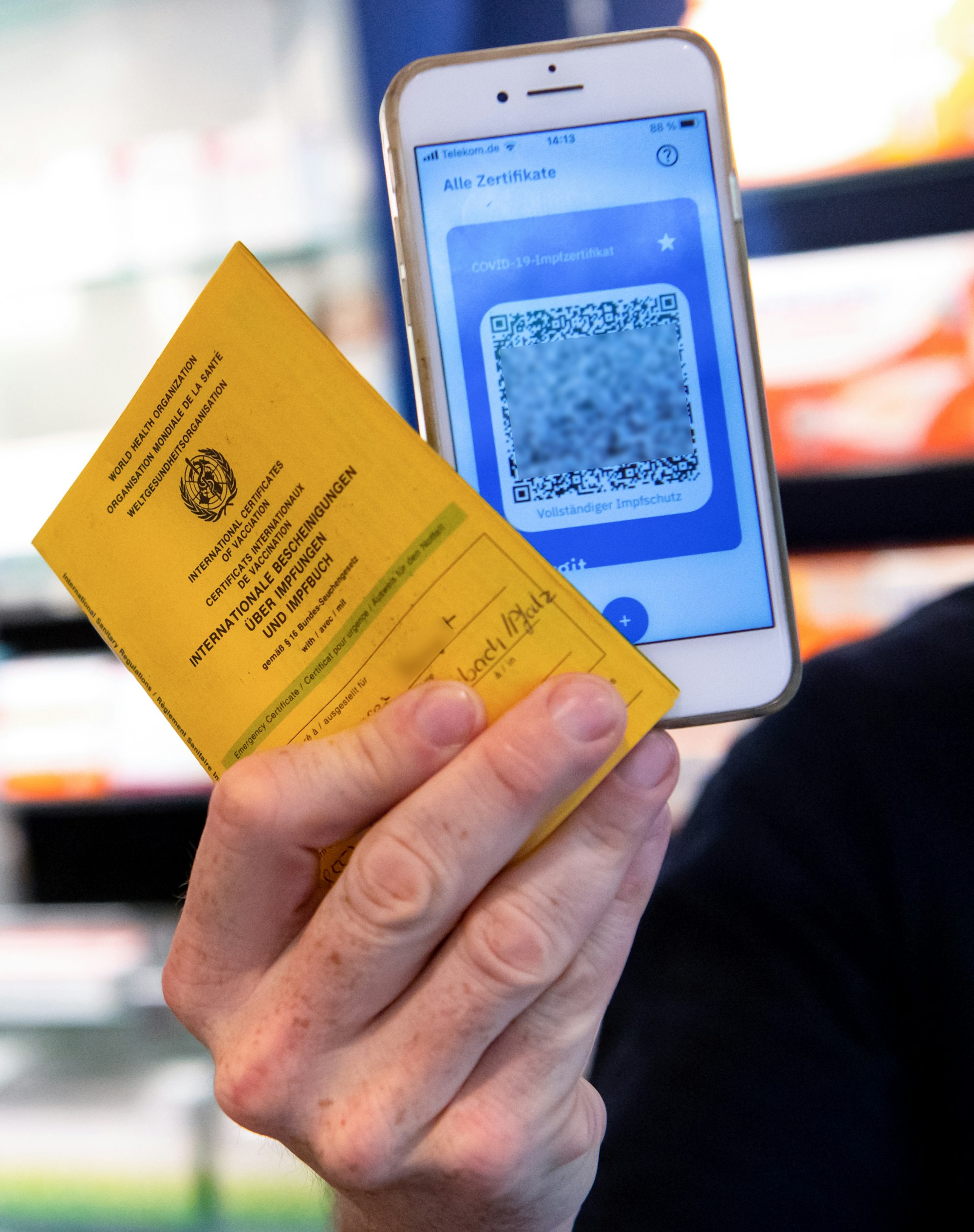 Ein Apotheker hält einen Impfpass und einen digitalen Impfnachweis in den Händen.
