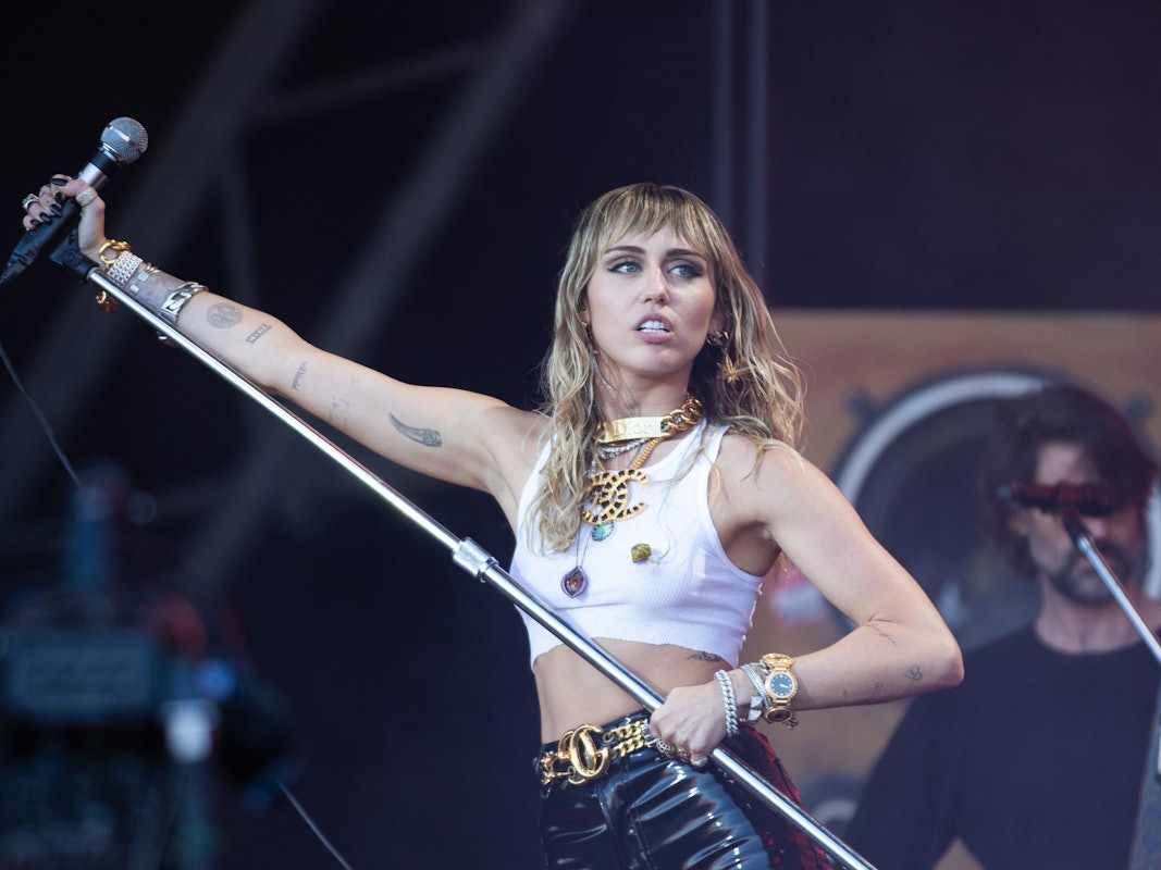 Miley Cyrus steht mit Mikrofonständer in der Hand bei einem Festival auf der Bühne.