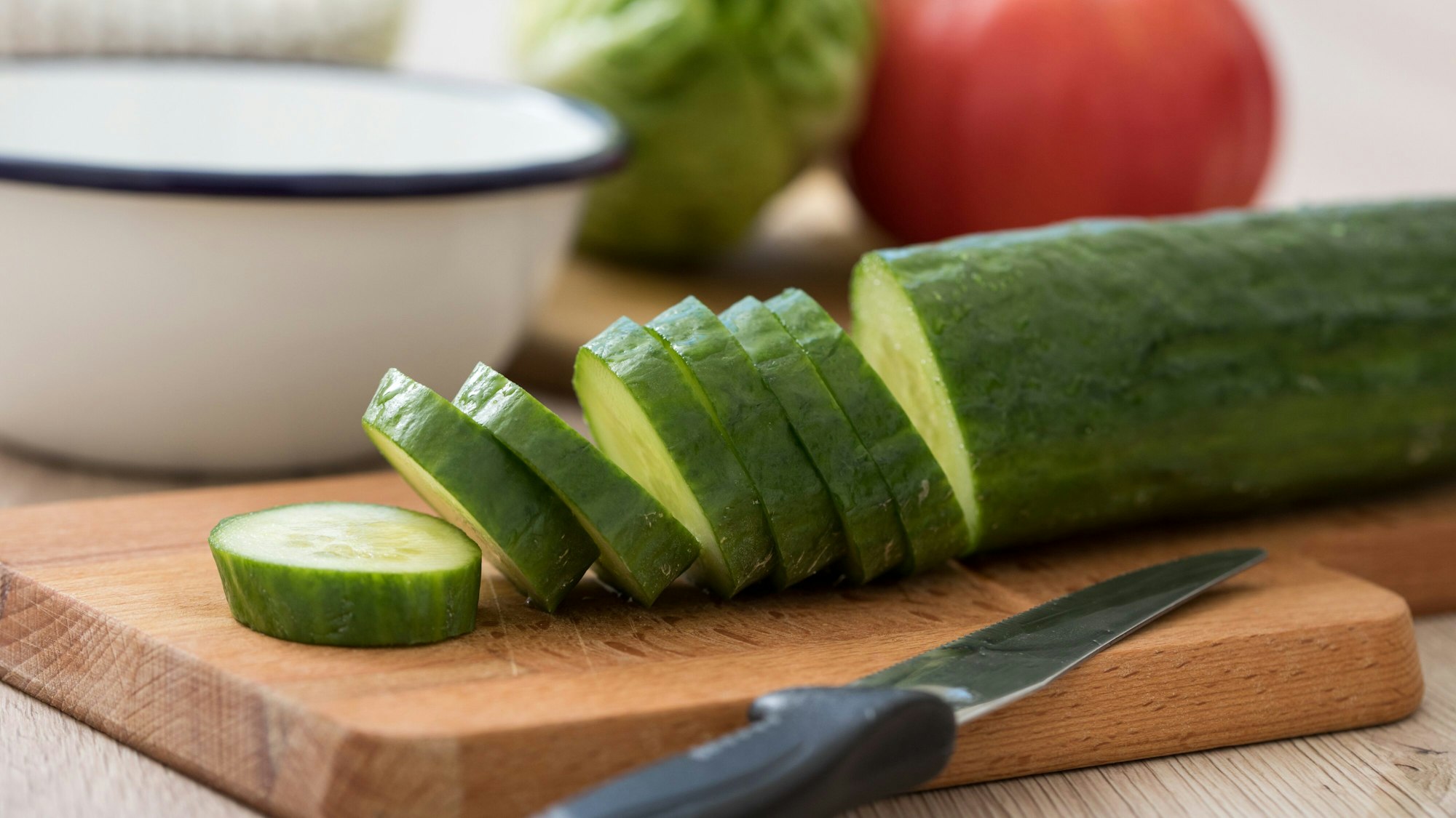 Eine Gurke ist auf einem Schneidebrett halb aufgeschnitten worden, das Messer liegt noch daneben.