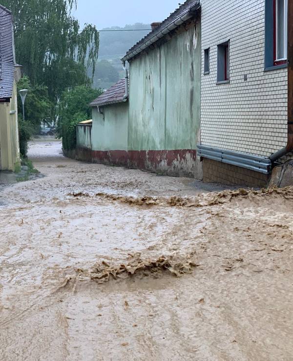Wassermassen fluten eine Straße und fließen an Häusern vorbei.