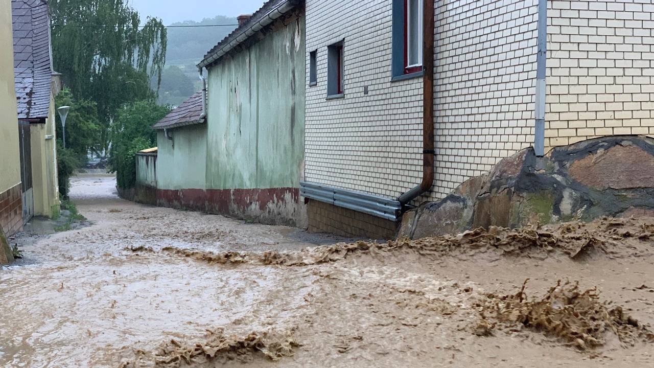 Wassermassen fluten eine Straße und fließen an Häusern vorbei.