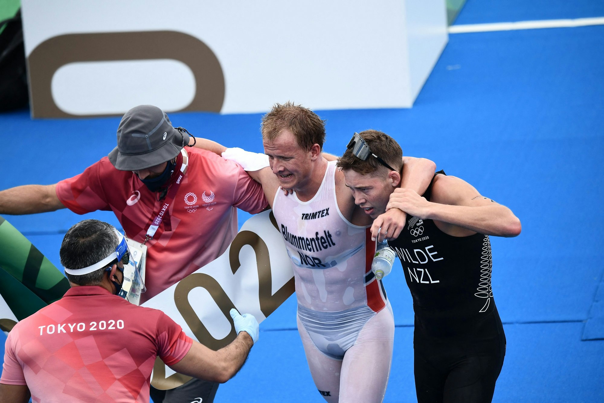 Gestützt vom Drittplatzierten Hayden Wilde und einem Betreuer verlässt Olympiasieger Blummenfelt den Zielbereich.