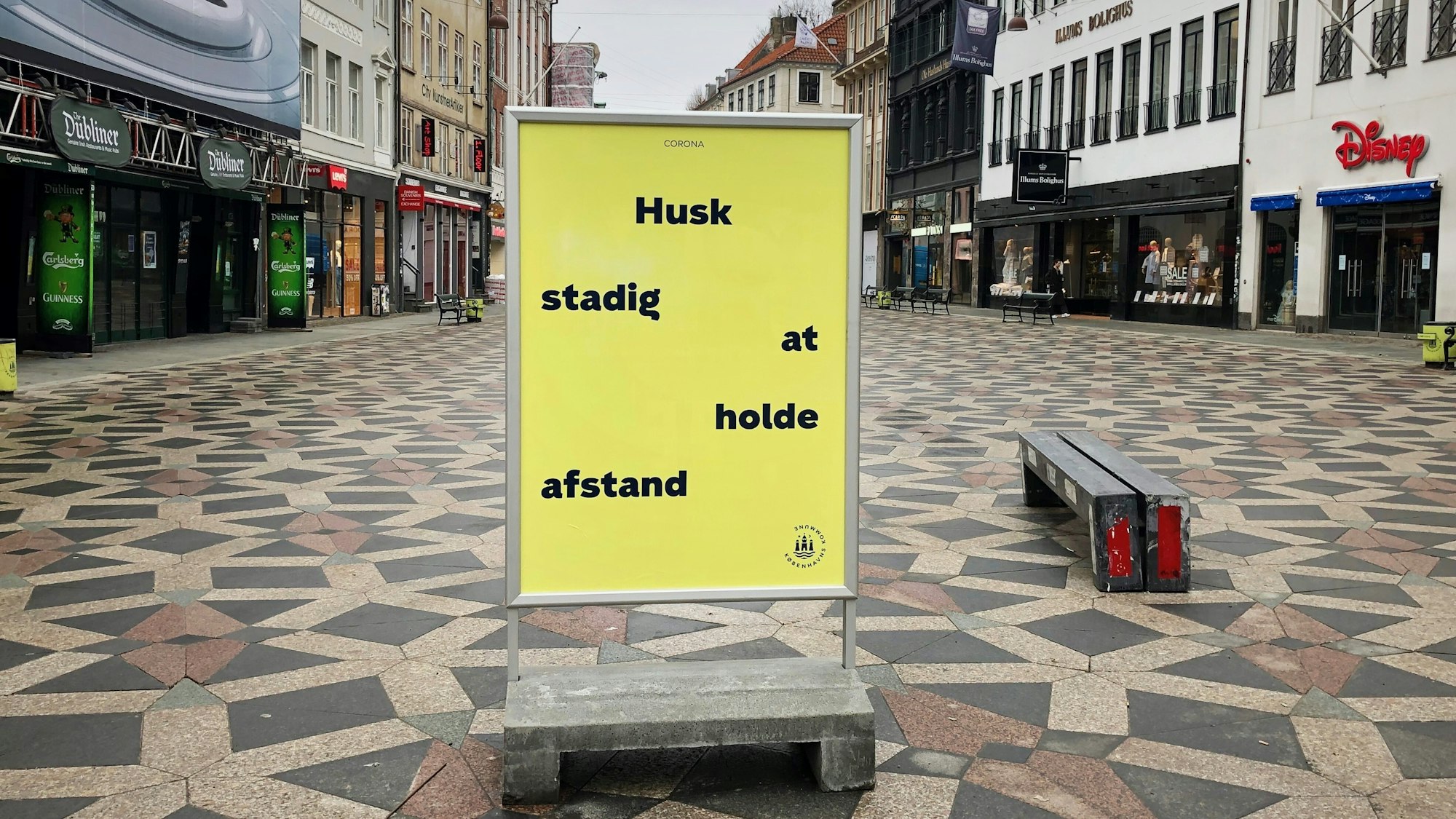 Auf einem Schild in der Fußgängerzone stehen die Worte: „Husk stadig at holde afstand”. Das ist dänisch und bedeutet: „Denken Sie daran, Abstand zu halten.”