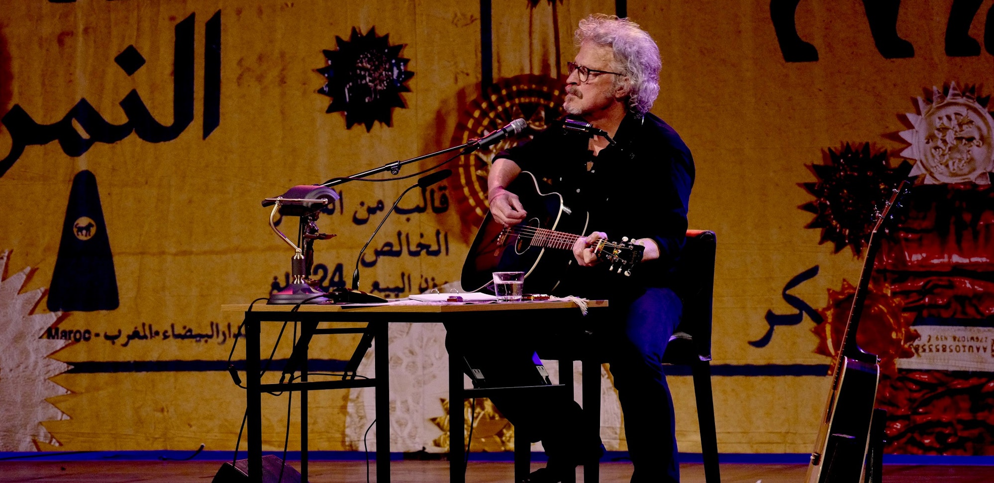 Wolfgang Niedecken spielt auf einer Bühne Gitarre und singt.