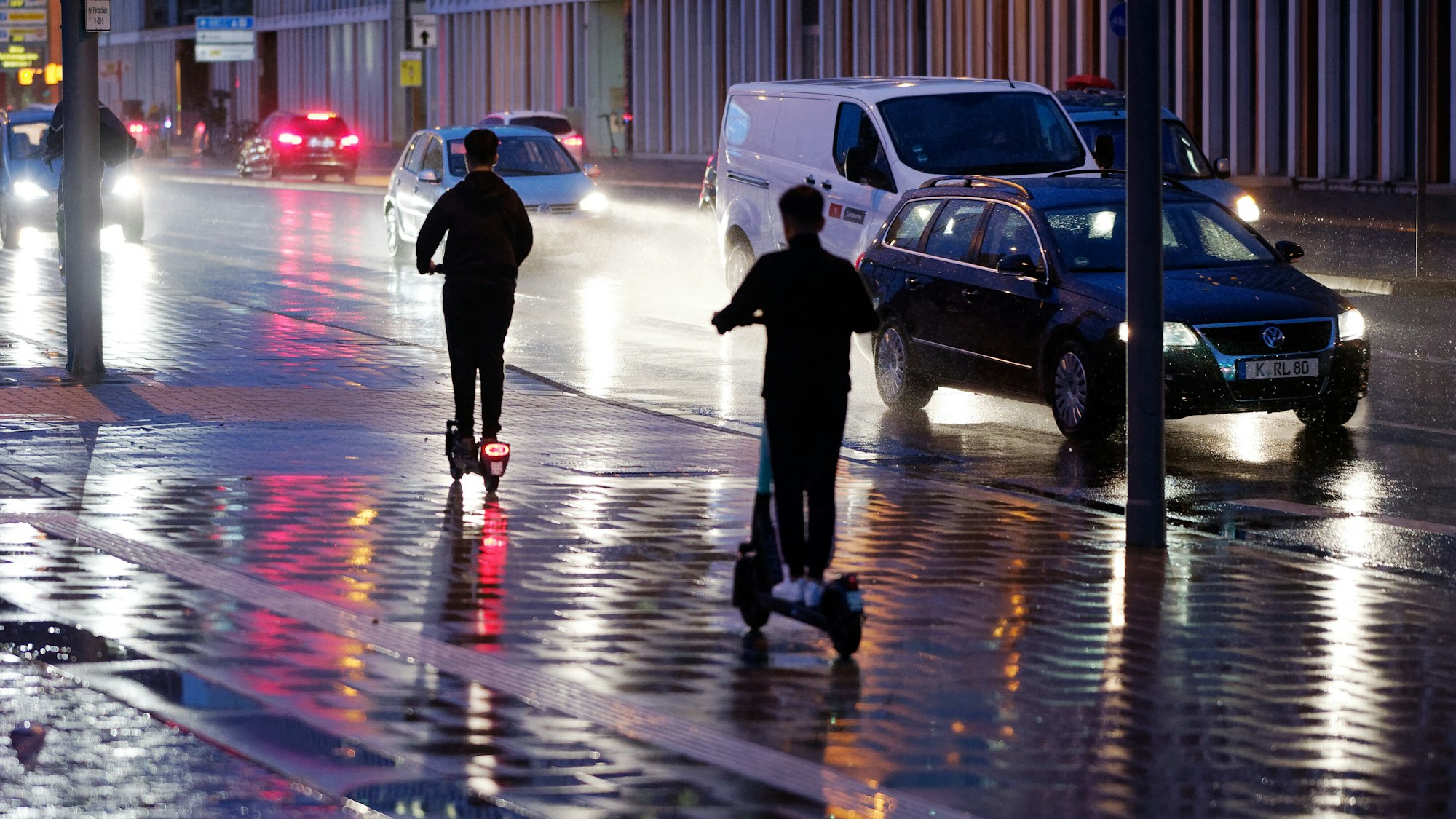 Junge Männer fahren bei Regen mit E-Scootern durch Köln.