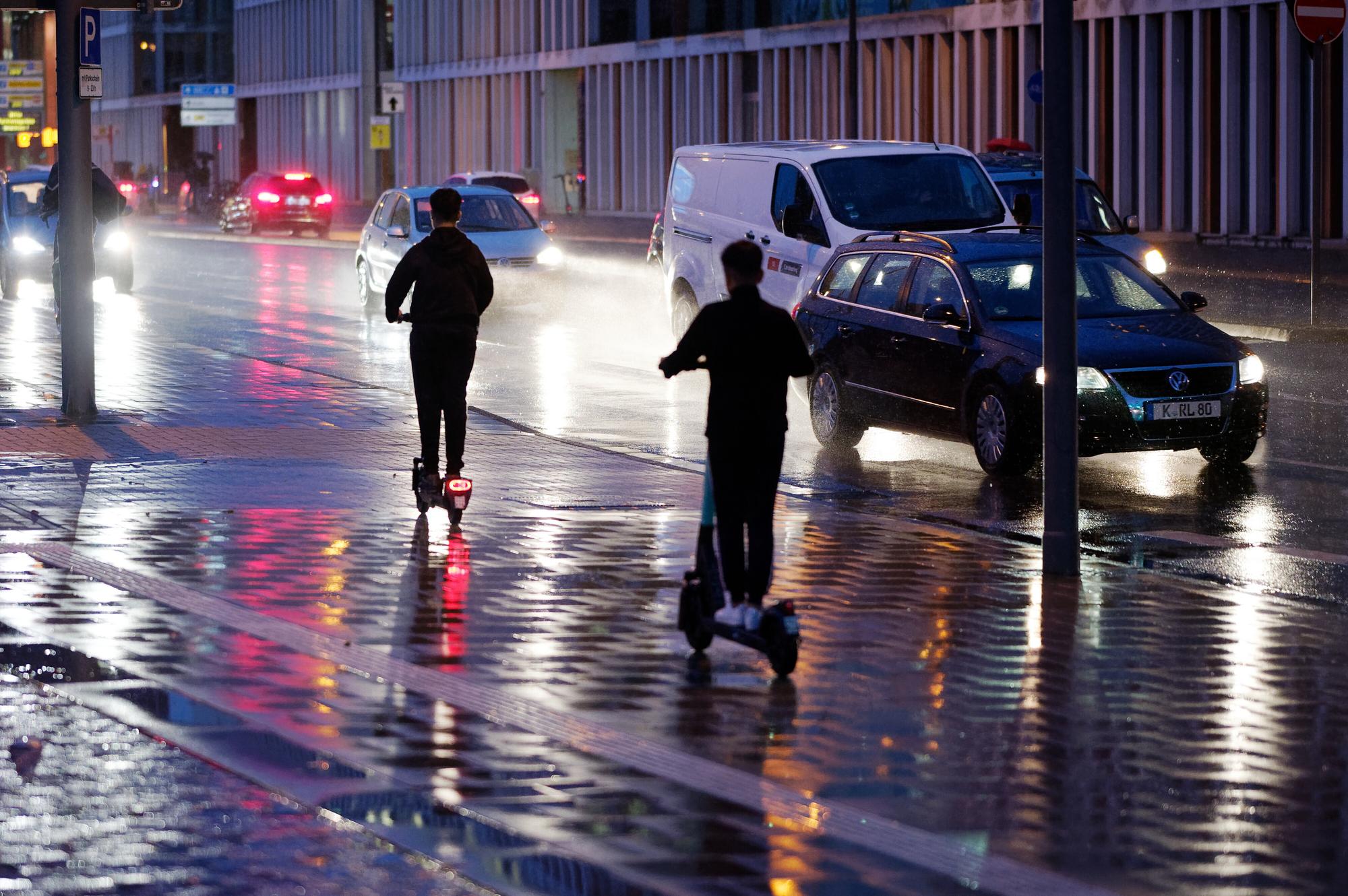 Junge Männer fahren bei Regen mit E-Scootern durch Köln.
