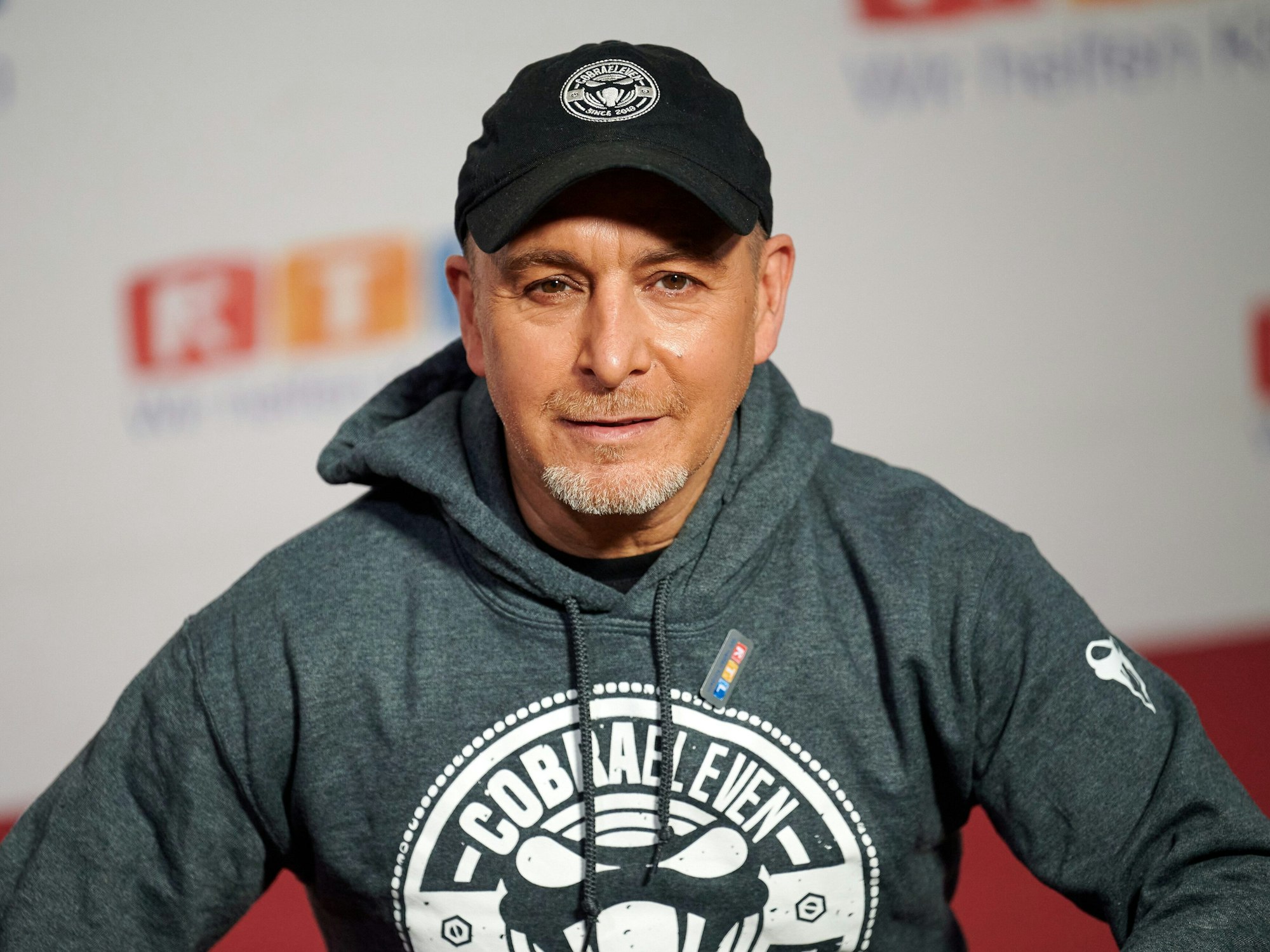 Der Schauspieler Erdogan Atalay sitzt beim 25. RTL Spendenmarathon vor einer Fotowand.