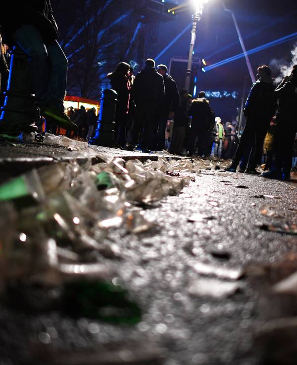 Auf einer Straße vor dem Brandenburger Tor liegen in der Silvesternacht 2017 Glasscherben. Im Hintergrund stehen Menschengruppen.
