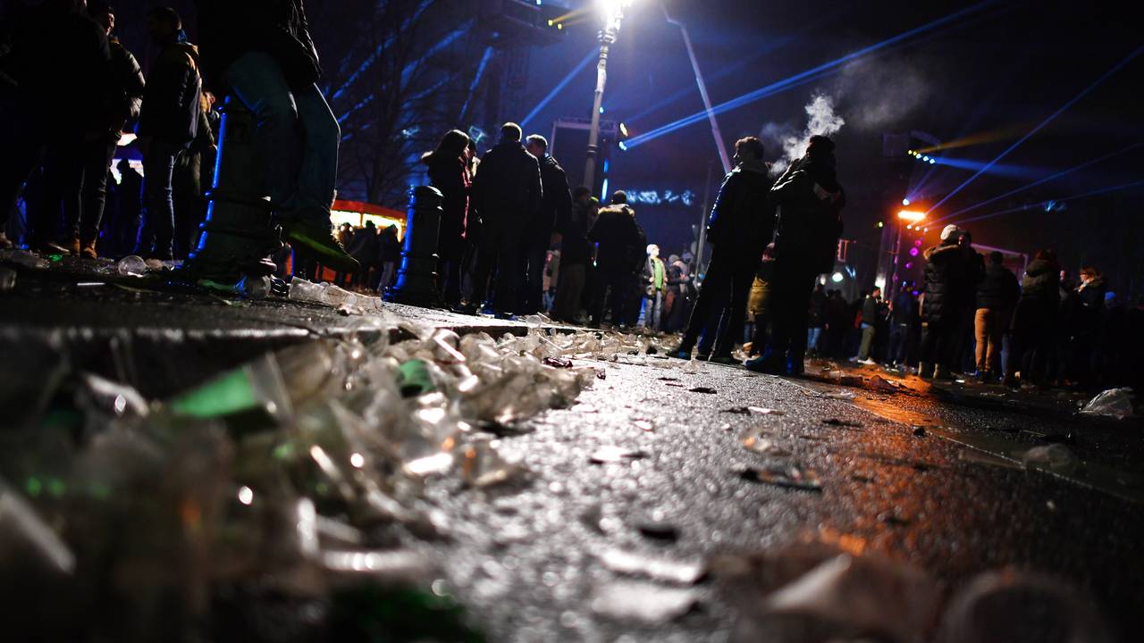 Auf einer Straße vor dem Brandenburger Tor liegen in der Silvesternacht 2017 Glasscherben. Im Hintergrund stehen Menschengruppen.