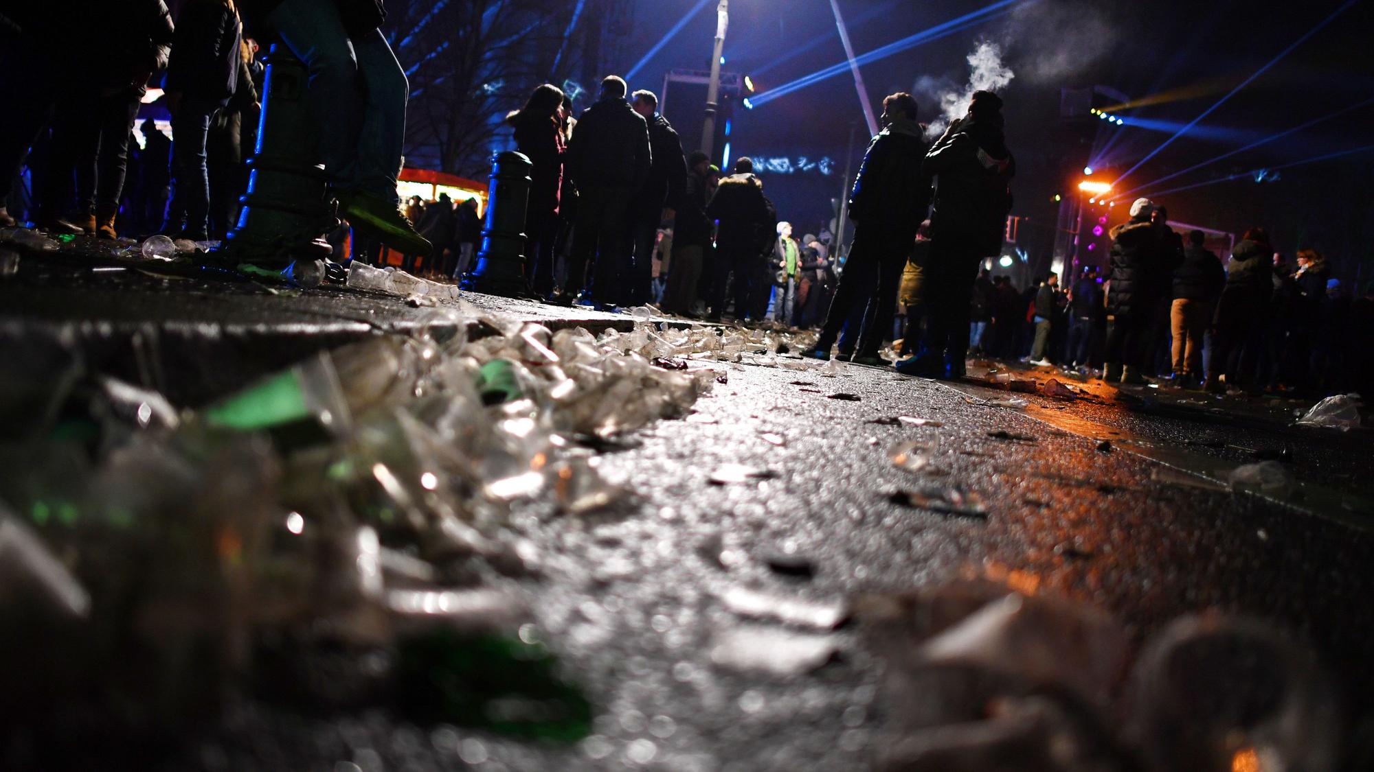 Auf einer Straße vor dem Brandenburger Tor liegen in der Silvesternacht 2017 Glasscherben. Im Hintergrund stehen Menschengruppen.