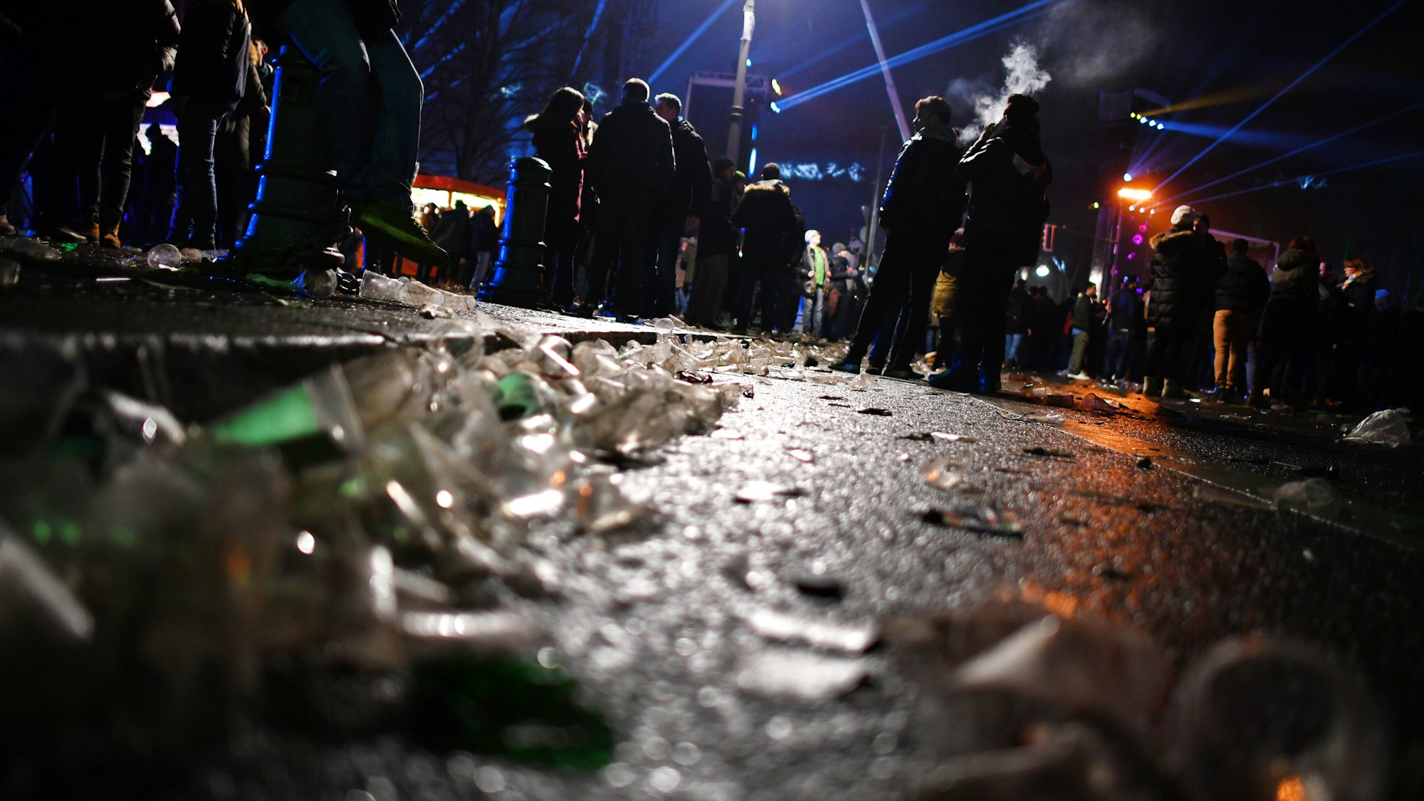Auf einer Straße vor dem Brandenburger Tor liegen in der Silvesternacht 2017 Glasscherben. Im Hintergrund stehen Menschengruppen.