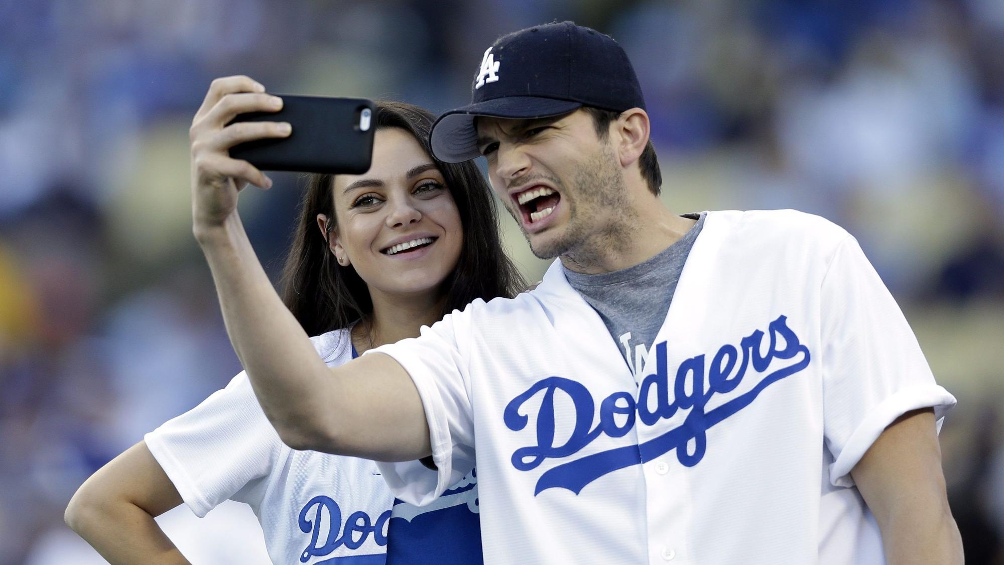 Ahston Kutcher macht ein Selfie von sich und Mila Kunis in Baseball-Outfits der Dodgers.