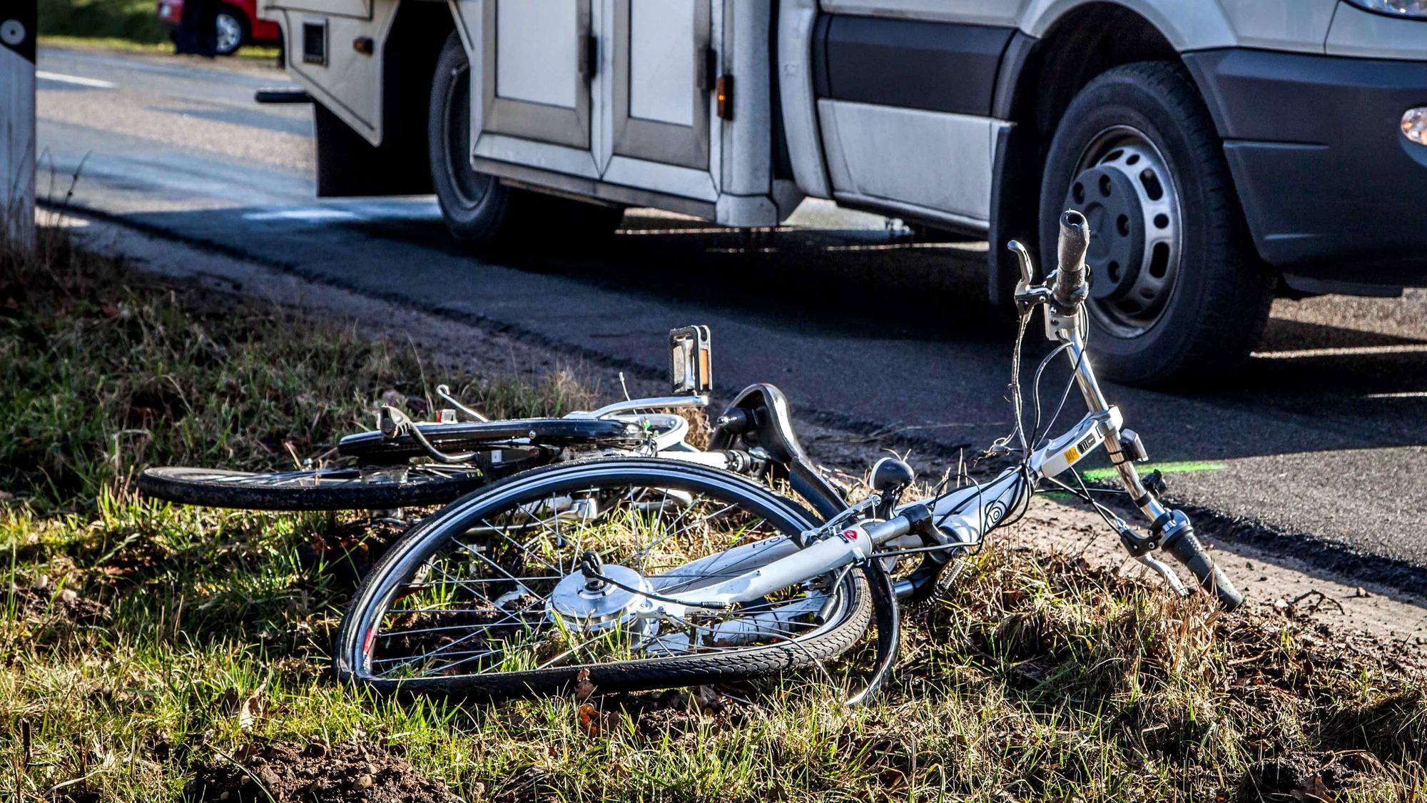 Ein zerstörtes Fahrrad liegt auf einer Straße. Im Hintergrund steht ein Rettungswagen.