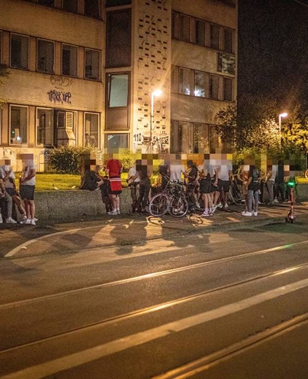 Auf einer Mauer an der Zülpicher Straße auf dem Universitätsgelände sitzen zahlreiche Menschen.