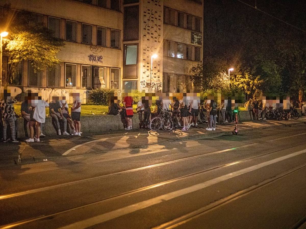 Auf einer Mauer an der Zülpicher Straße auf dem Universitätsgelände sitzen zahlreiche Menschen.