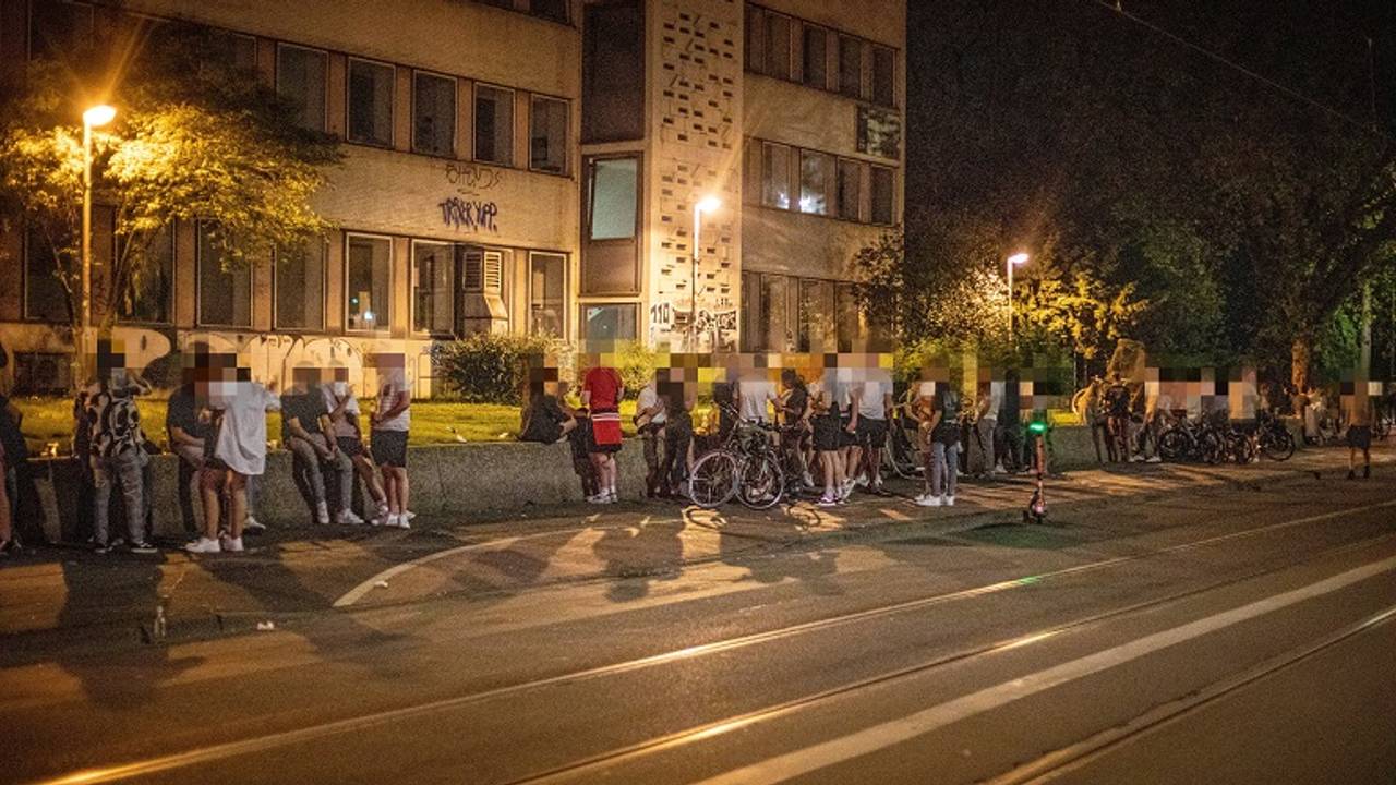 Auf einer Mauer an der Zülpicher Straße auf dem Universitätsgelände sitzen zahlreiche Menschen.