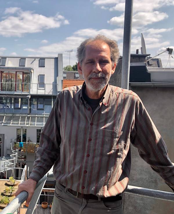 Architekt Gabor Schneider steht auf einem Balkon, der sich noch im Rohbau befindet. Im Hintergrund der Dachgarten und das Wohnhaus.