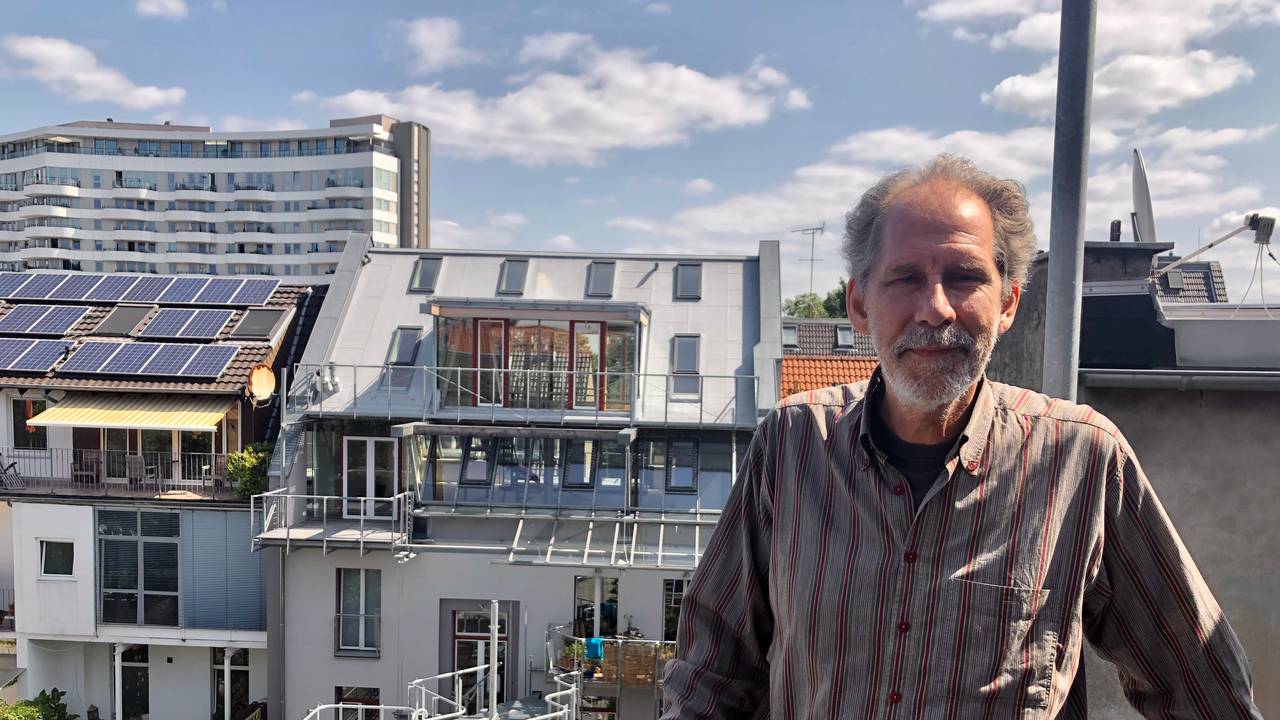 Architekt Gabor Schneider steht auf einem Balkon, der sich noch im Rohbau befindet. Im Hintergrund der Dachgarten und das Wohnhaus.