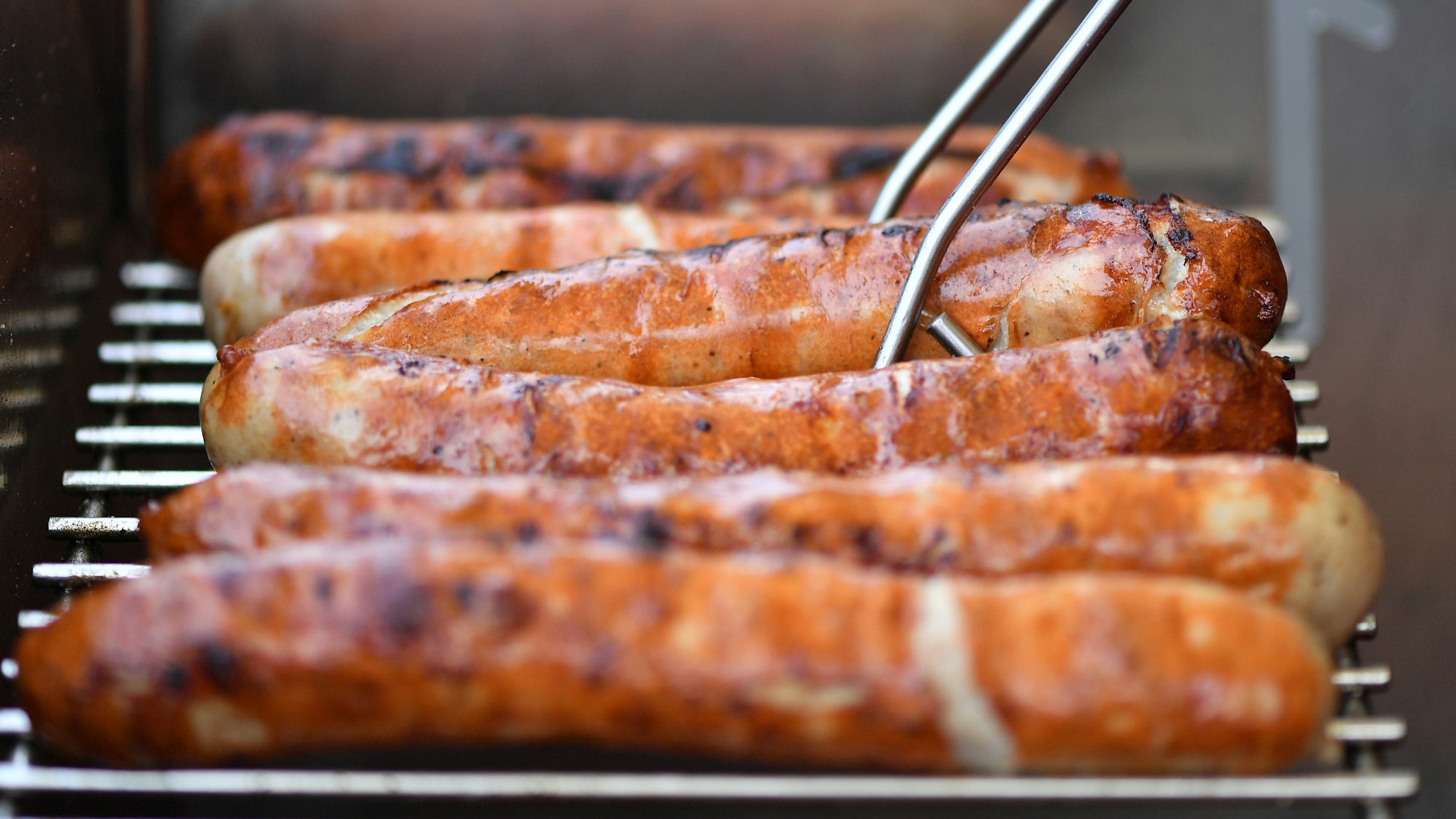Auf einem Grill liegen sechs braun gebrutzelte Thüringer Bratwürste nebeneinander.
