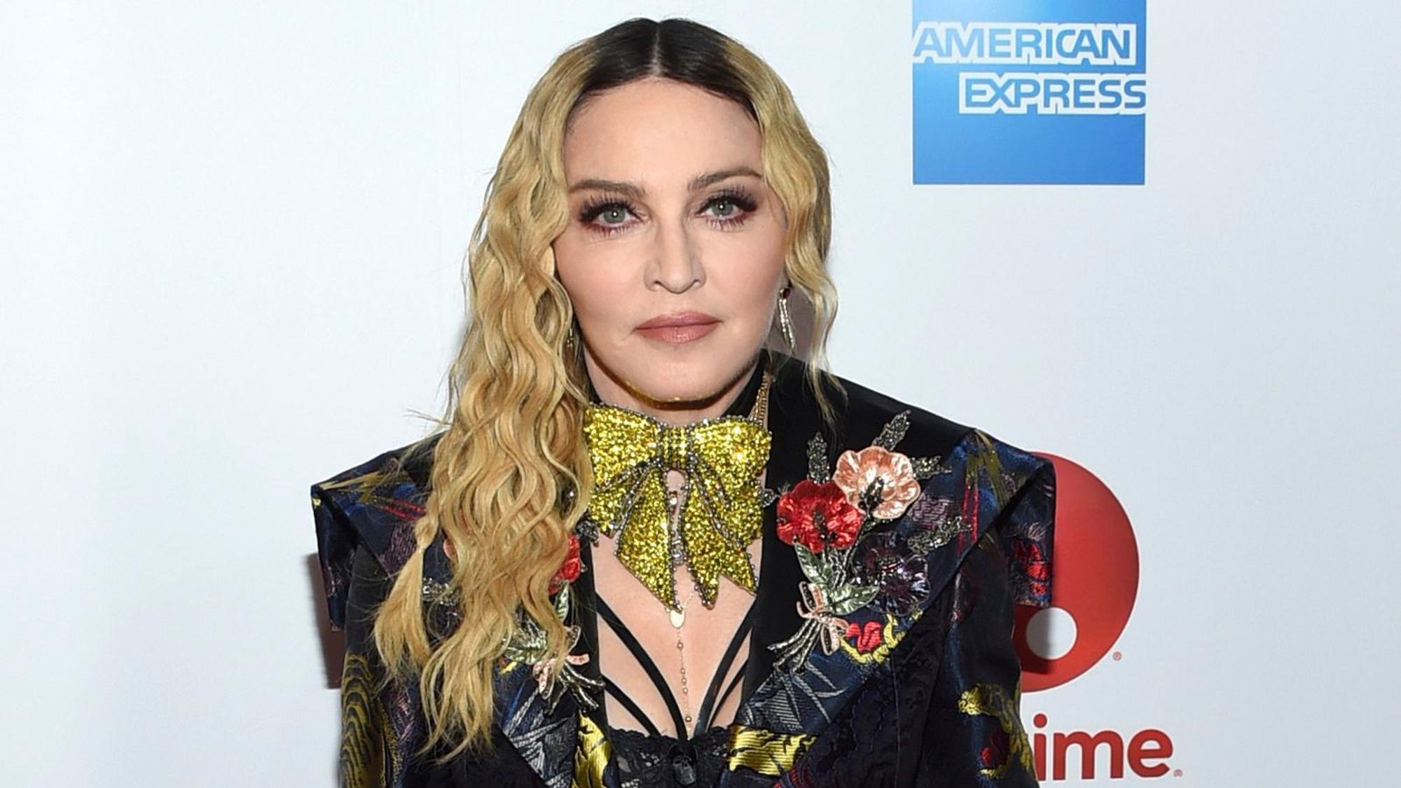 Madonna posiert im schwarzen Anzug mit auffälliger goldener Schleife um den Hals.