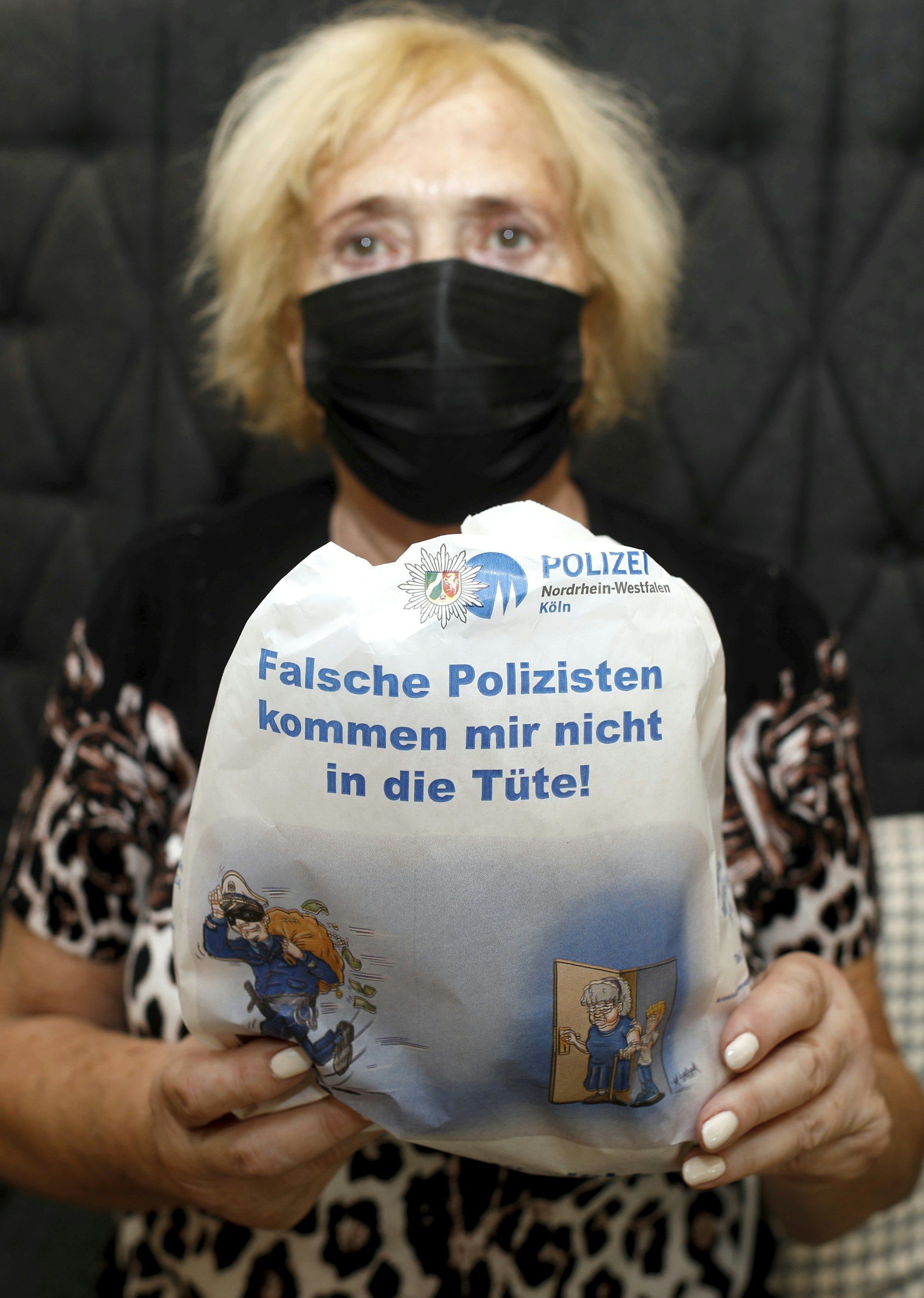 Frau zeigt Brötchen-Tüte mit Hinweis auf falsche Polizisten.