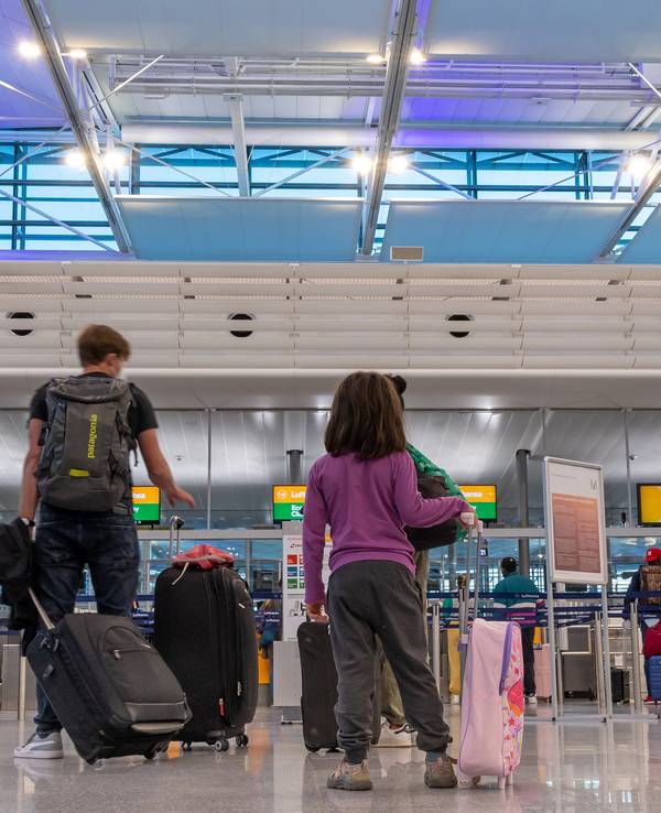 Passagiere stehen am Flughafen München an einem Check-In-Schalter.