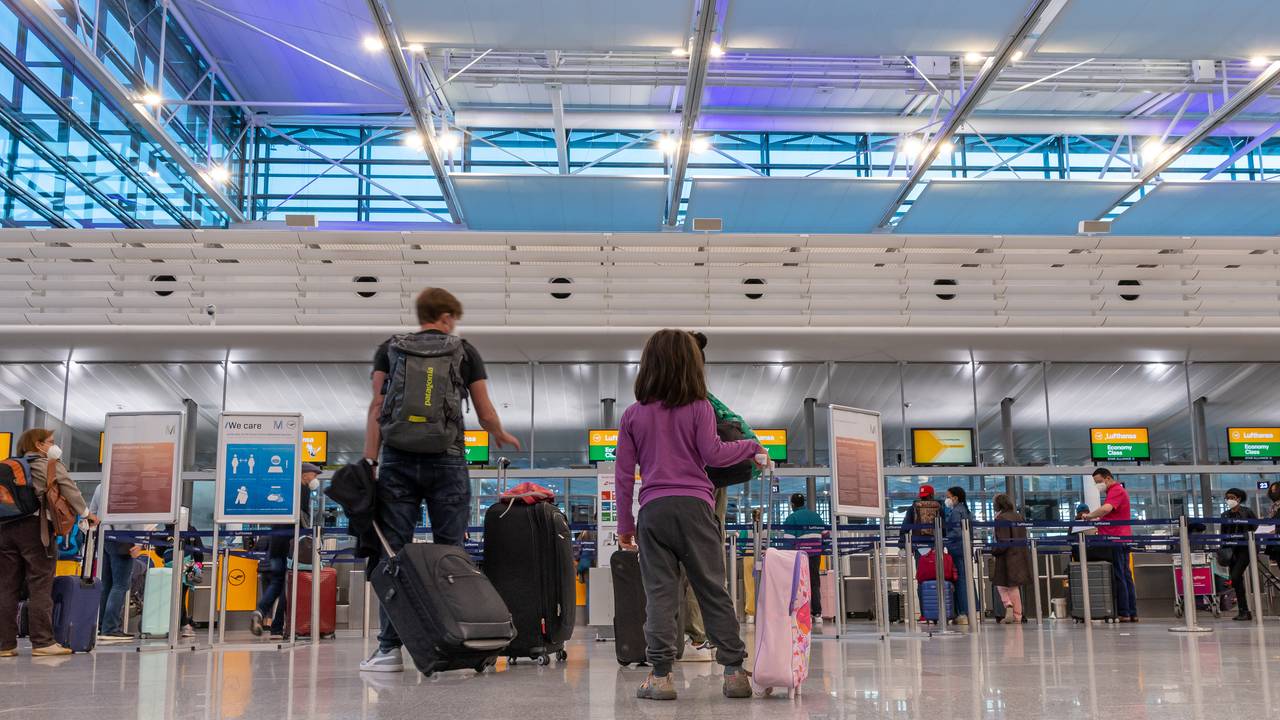 Passagiere stehen am Flughafen München an einem Check-In-Schalter.