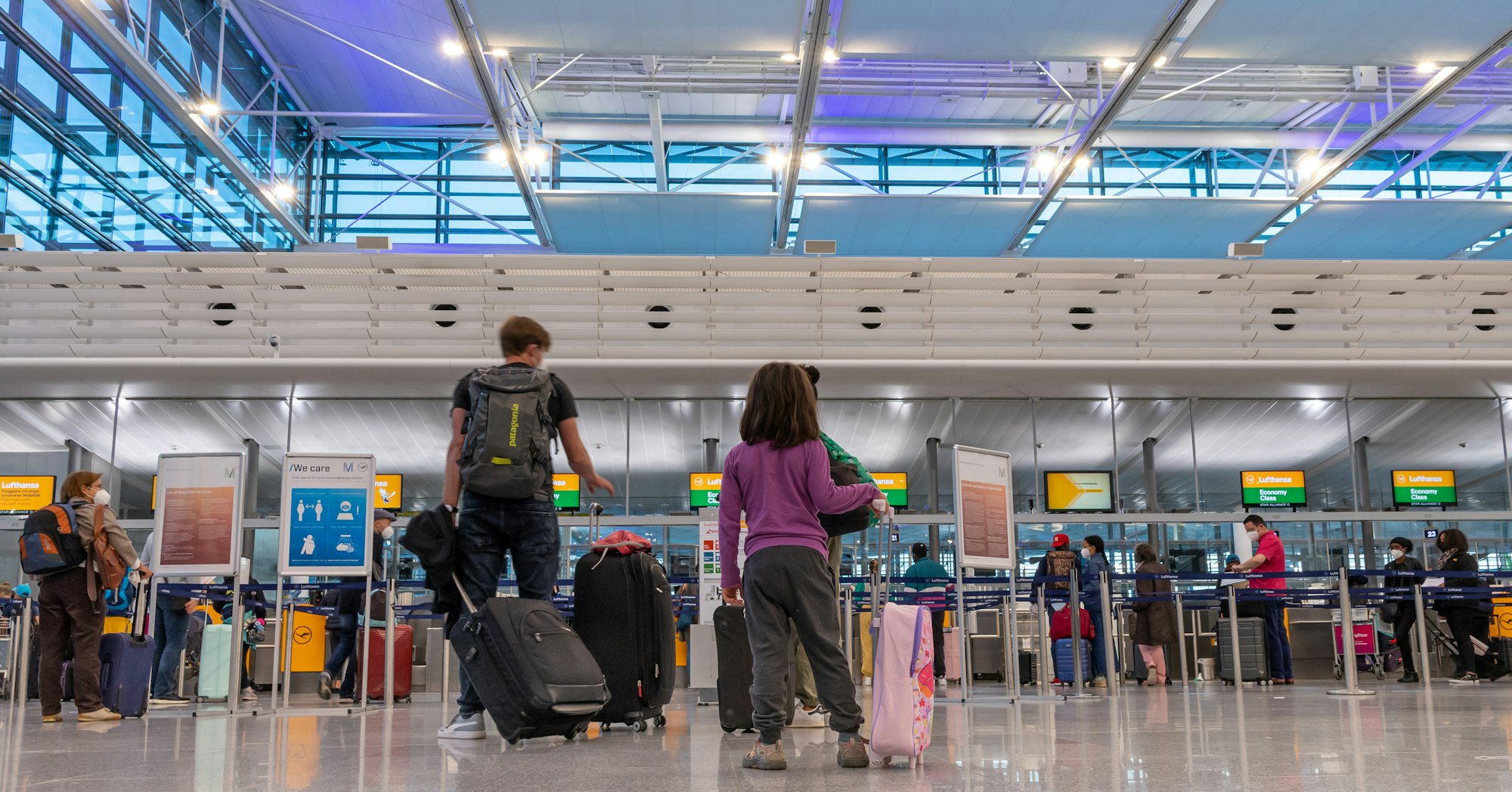Passagiere stehen am Flughafen München an einem Check-In-Schalter.