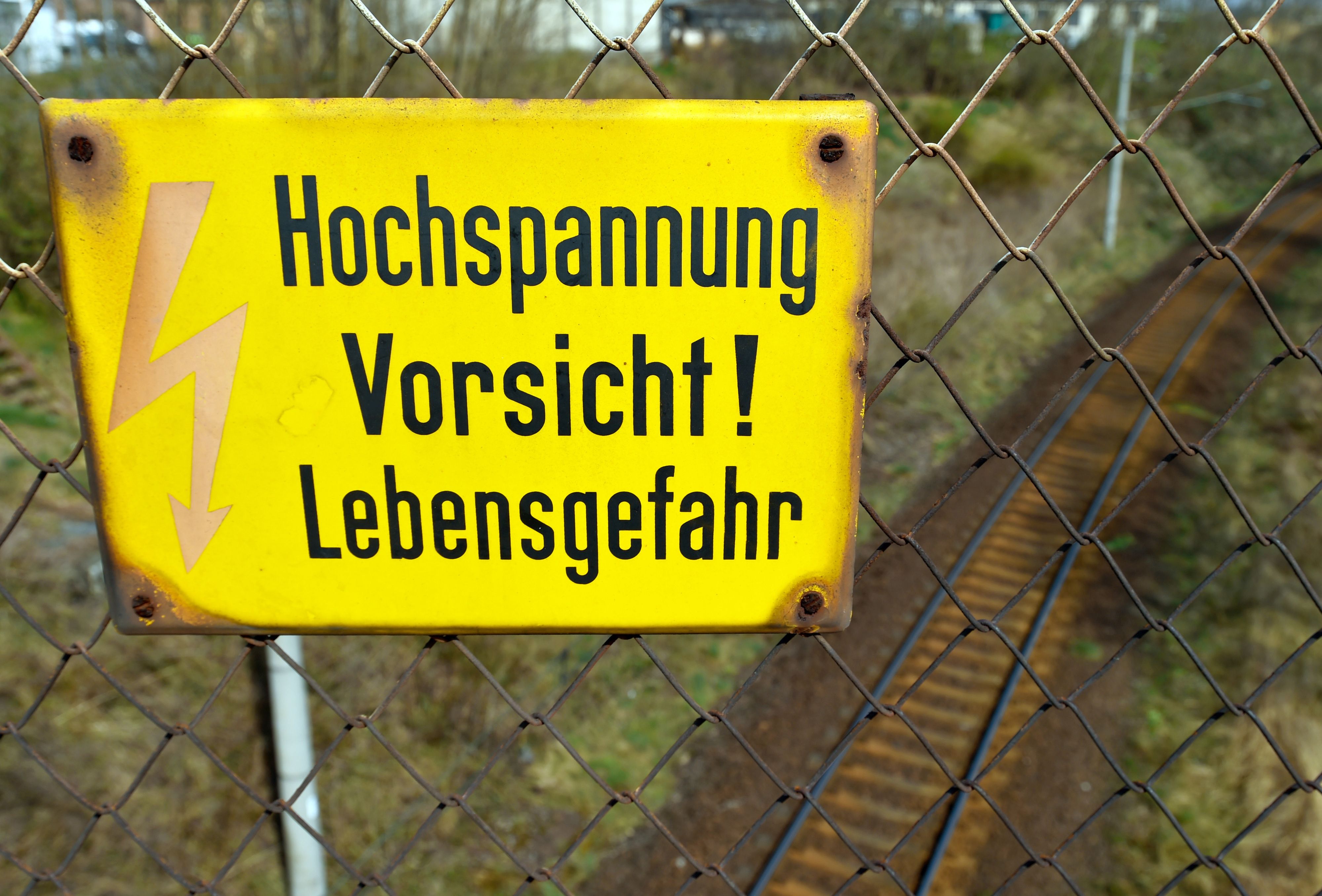 Das Symbolfoto zeigt ein deutsches Hinweisschild, das an einem Zaun hängt. Auf dem steht mit schwarz auf gelbem Untergrund „Hochspannung Vorsicht! Lebensgefahr”.