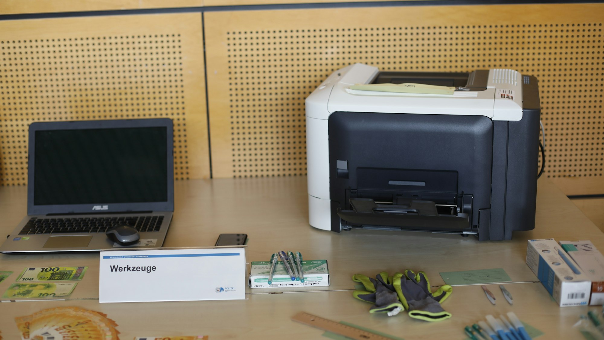 Auf einem Tisch stehen das Werkzeug der Falschgeld-Produzenten, ein normaler Drucker und ein Laptop.