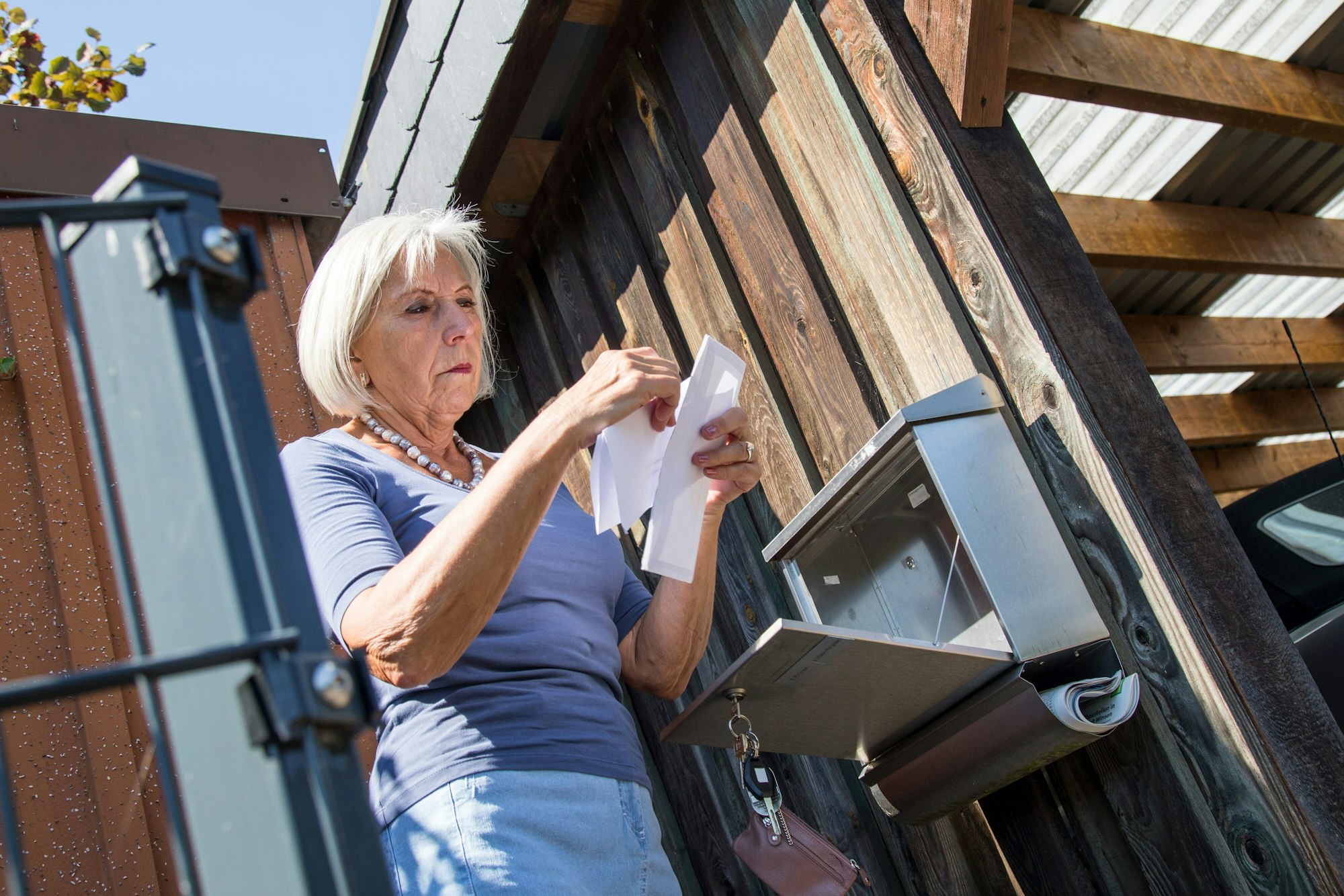 Eine ältere Dame steht am Briefkasten und sieht ihre Post durch. (Symbolfoto).