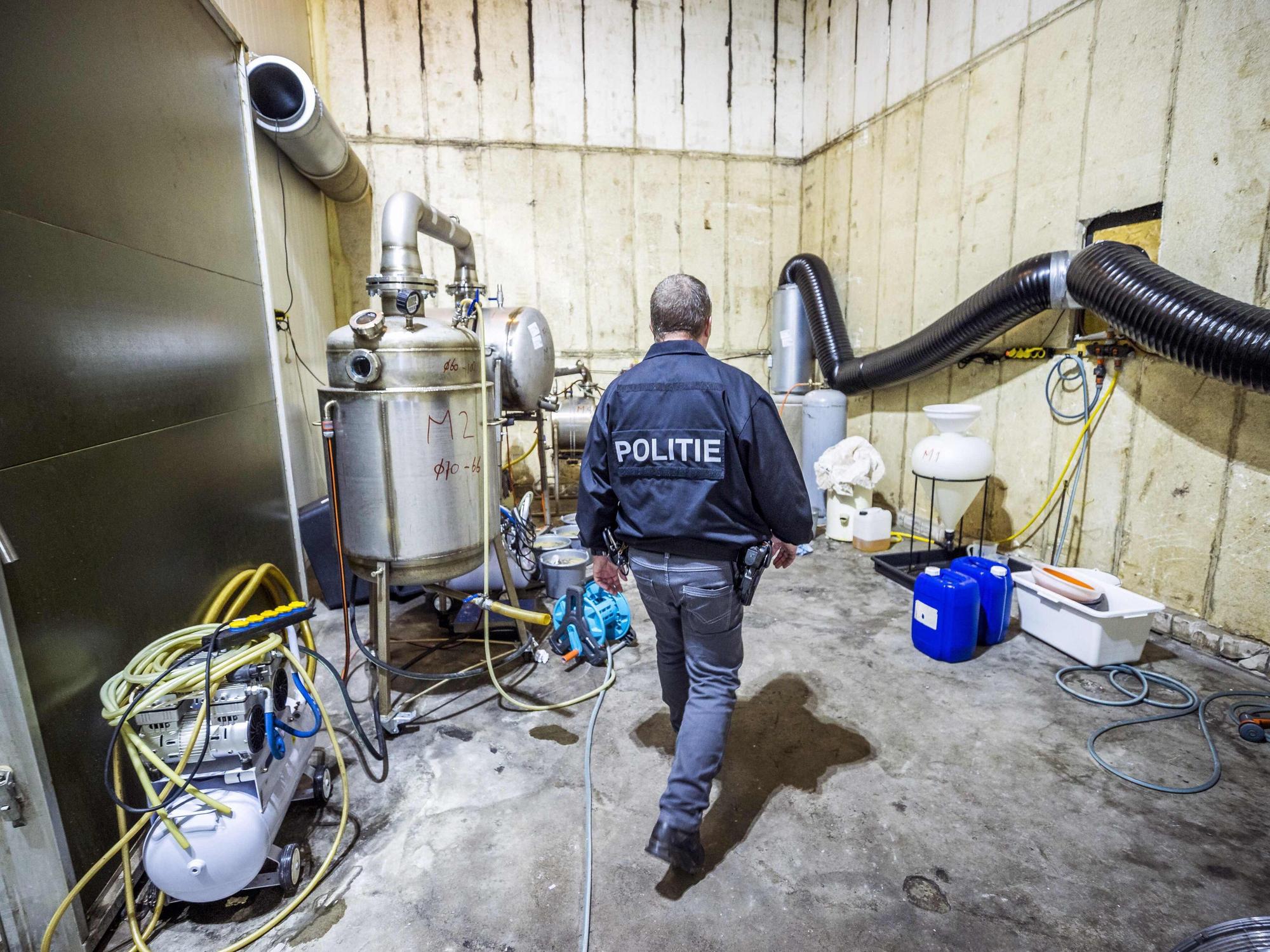 In einem Lagerraum stehen Apparate zur Herstellung chemischer Drogen. Ein Polizei-Beamter läuft durch das Labor.