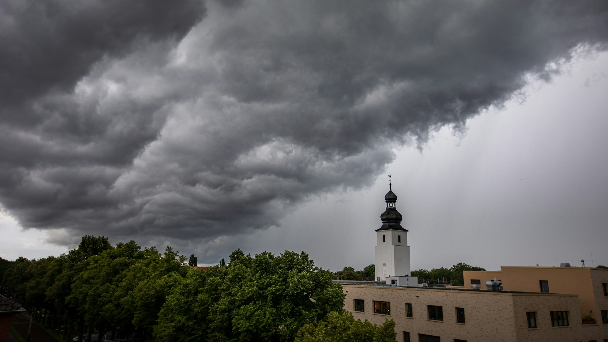 04.07.2021, Köln: Dunkle Wolken ziehen kurz vor einem Gewitter mit Starkregen über den Ortsteil Sülz. Der Kirchturm rechts gehört zur Kirche „Zur heiligen Familie“. Im Rheinland kommt es zu Unwettern. Foto: Matthias Heinekamp