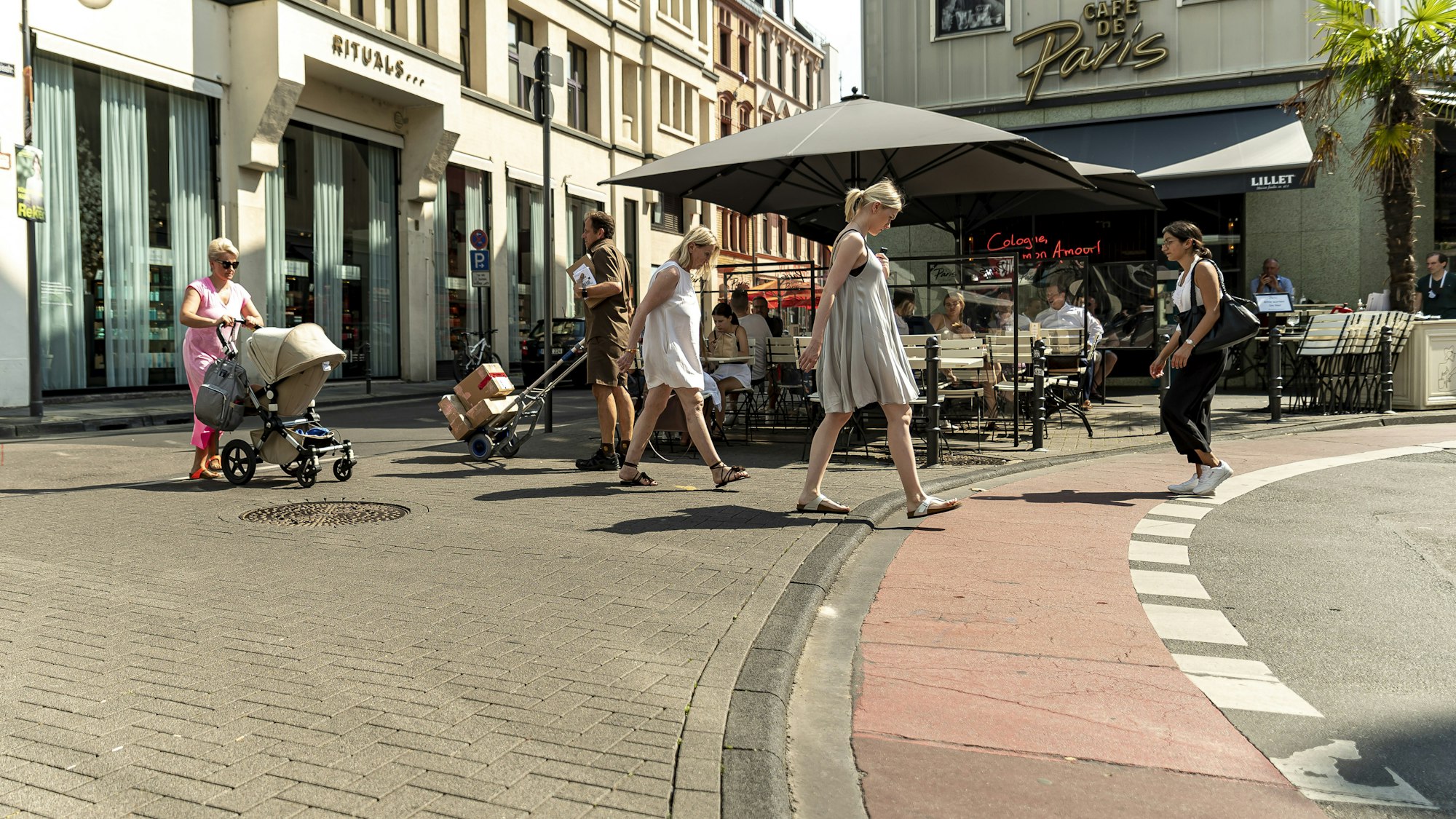 Passanten gehen auf der Ehrenstraße am Café de Paris vorbei
