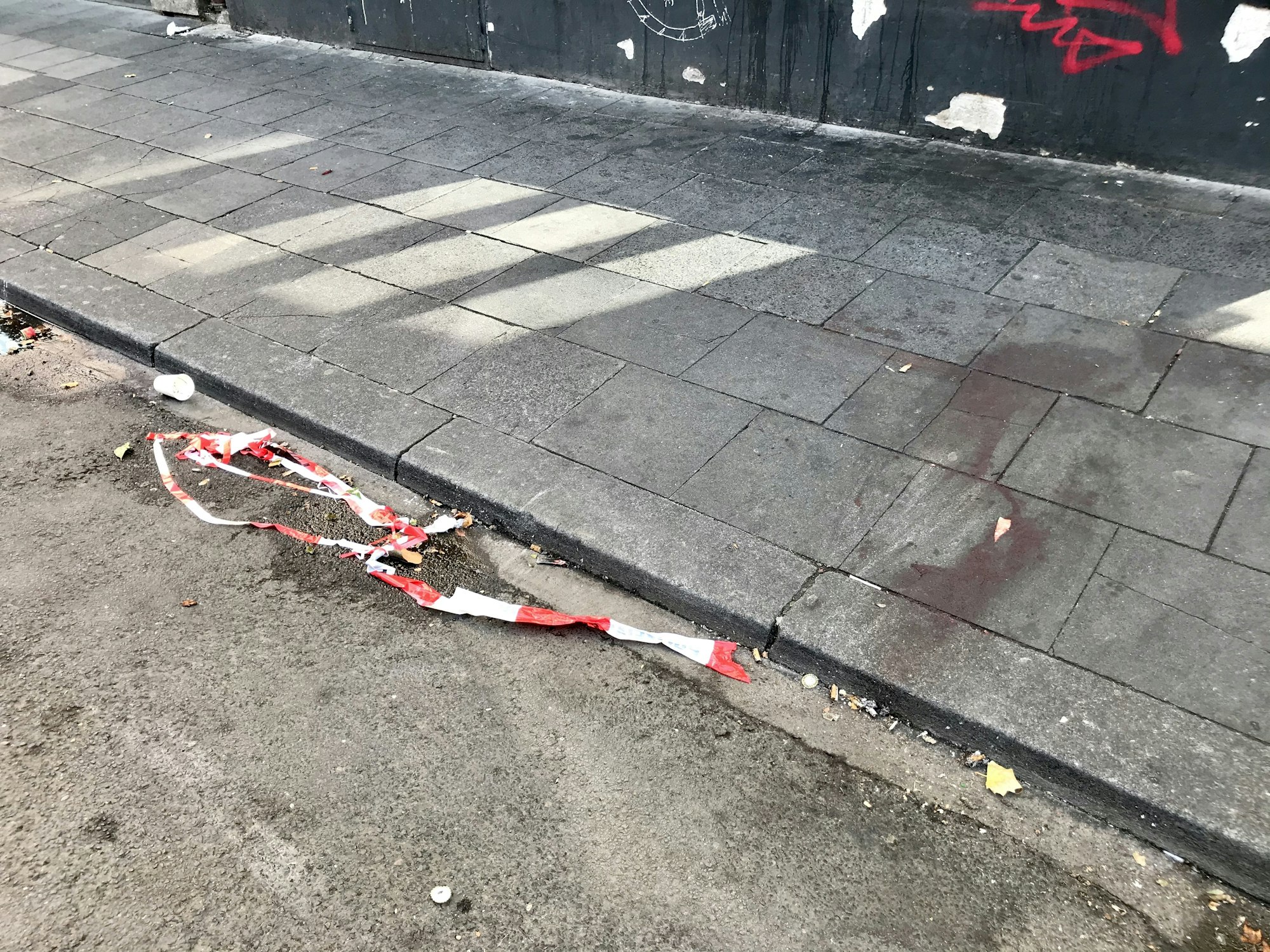 Blutspuren haften auf dem Bürgersteig der Zülpicher Straße, davor liegen Reste eines Flatterbands.