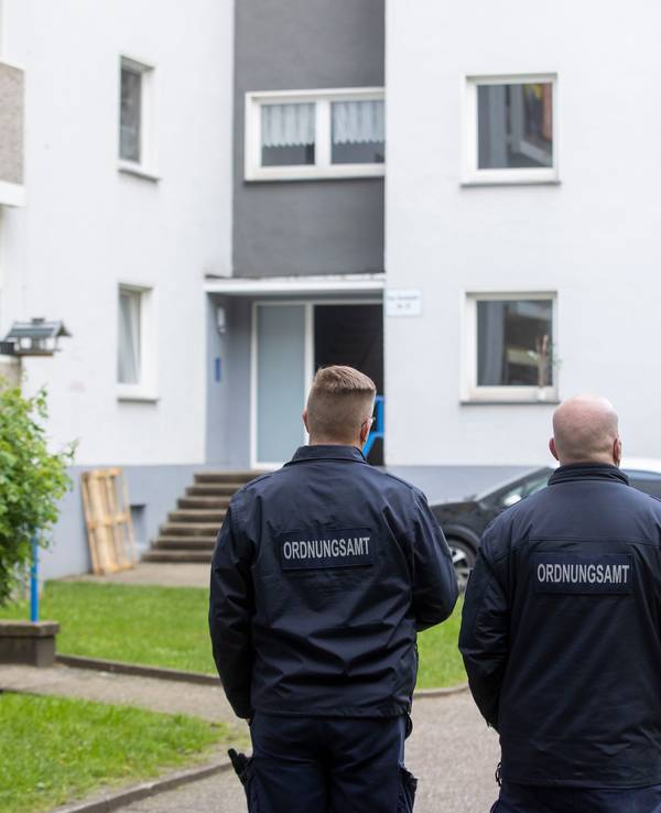 Mitarbeiter des Ordnungsamt stehen vor einem Eingang eines Hochhauses.