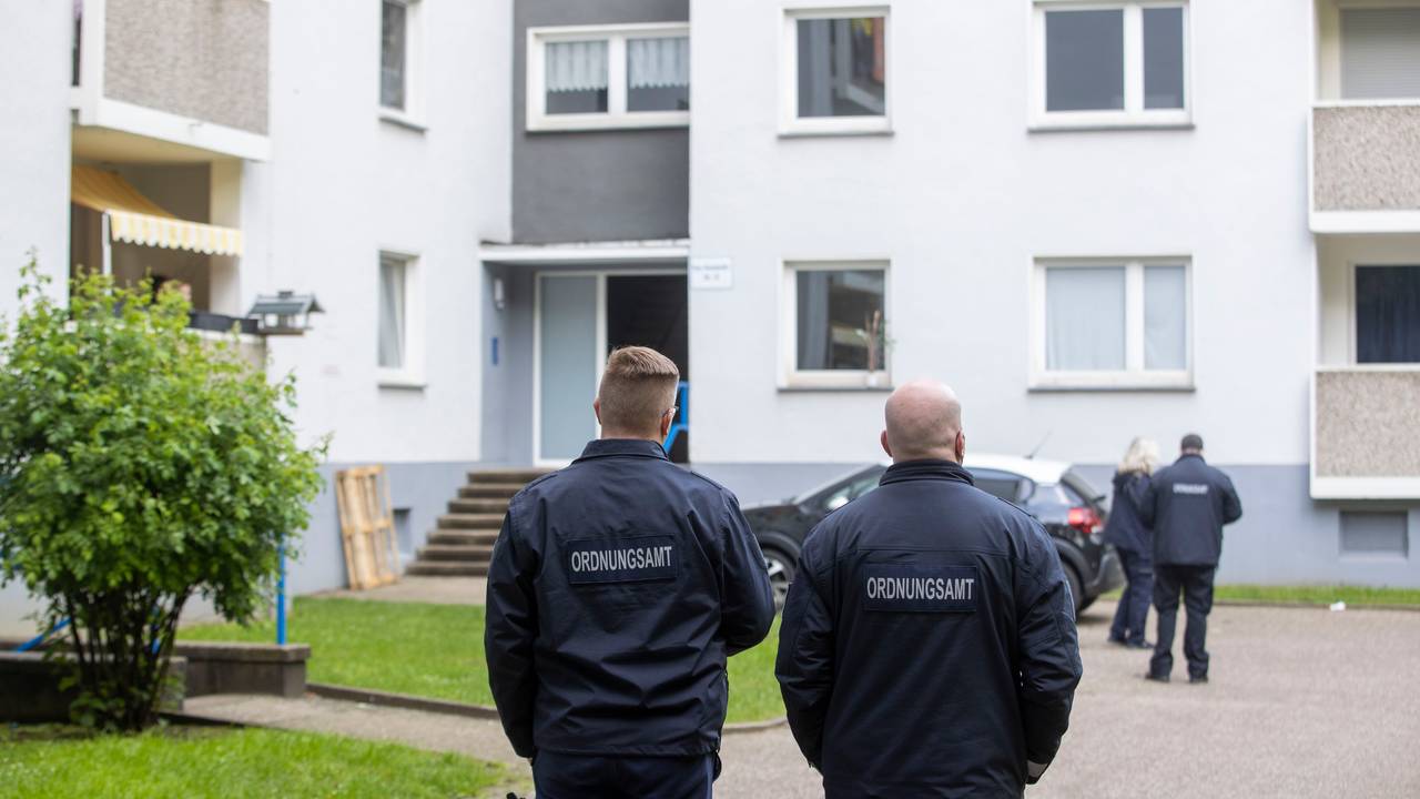 Mitarbeiter des Ordnungsamt stehen vor einem Eingang eines Hochhauses.