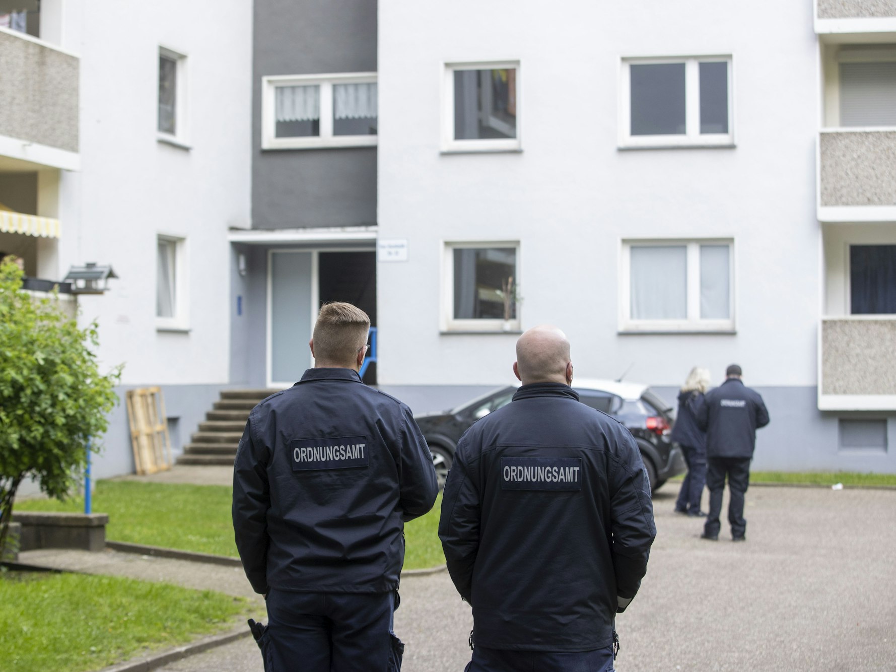 Mitarbeiter des Ordnungsamt stehen vor einem Eingang eines Hochhauses.