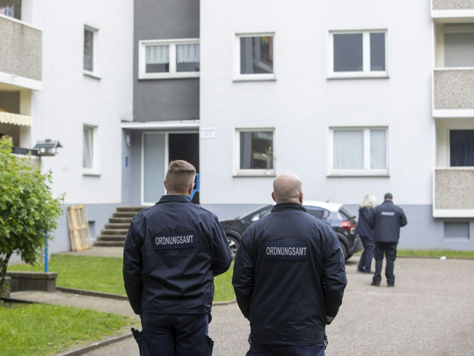 Mitarbeiter des Ordnungsamt stehen vor einem Eingang eines Hochhauses.