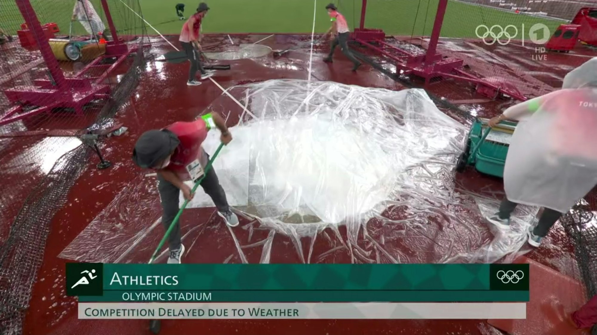 Mit Besen und Walzen räumen Helfer Wasser von den Anlagen im Olympiastadion in Tokio.