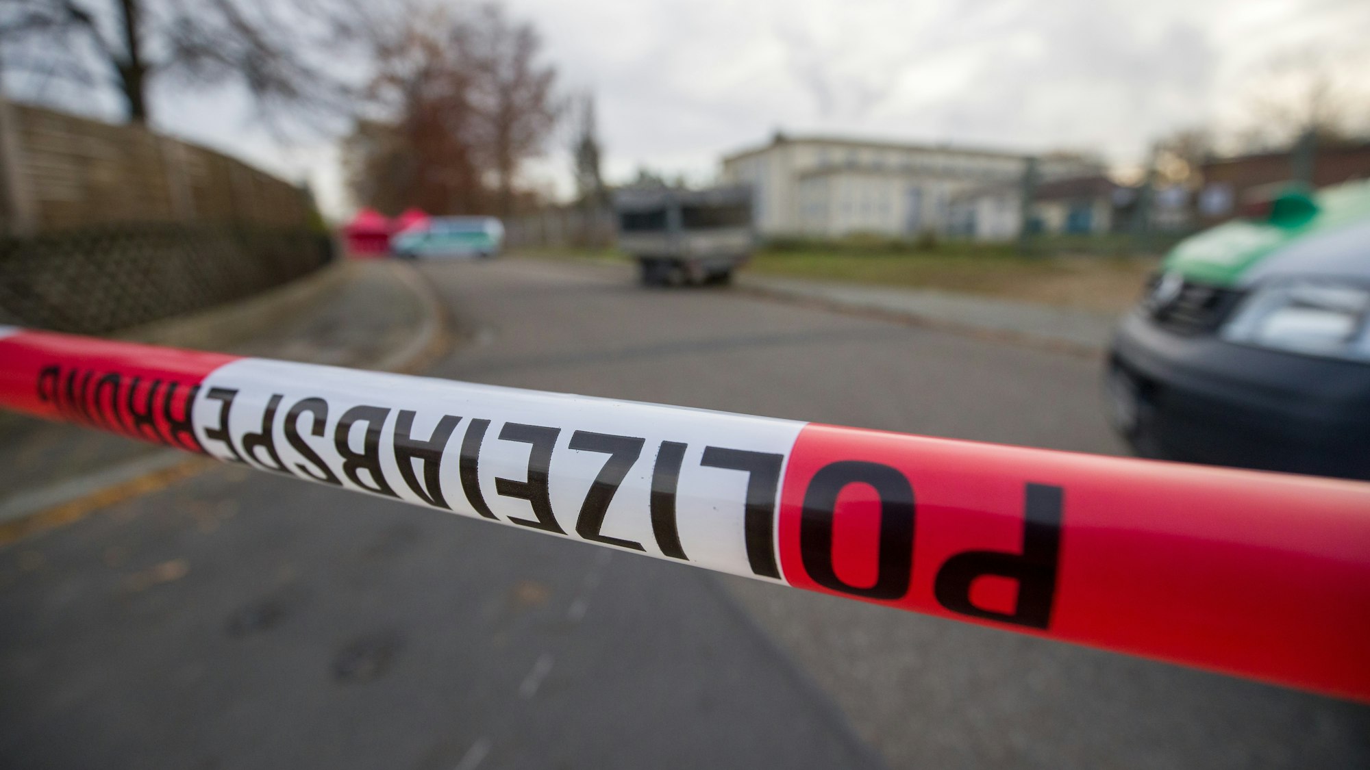 Ein rot-weißes Flatterband mit der Aufschrift Polizeiabsperrung vor einem Einsatzwagen der Polizei.