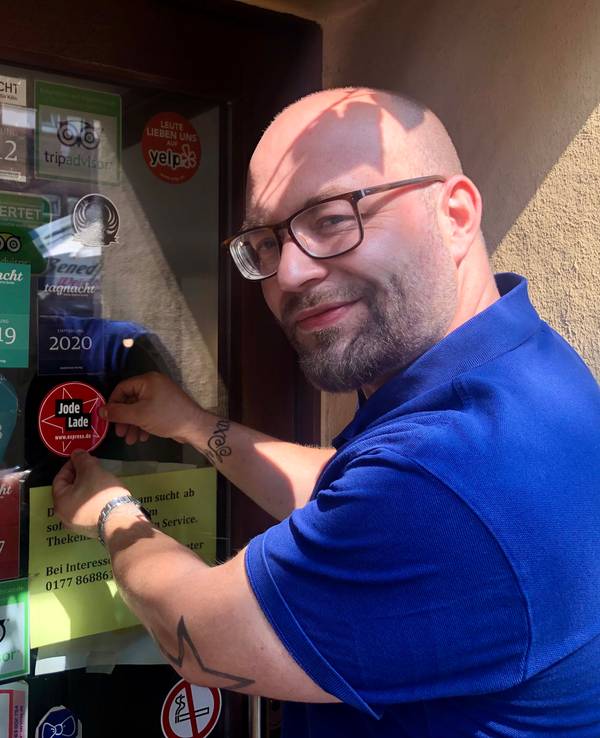Geschäftsführer Janis Ruhbach klebt den „Jode Lade“-Sticker an die Eingangstür des „Caminetto“.