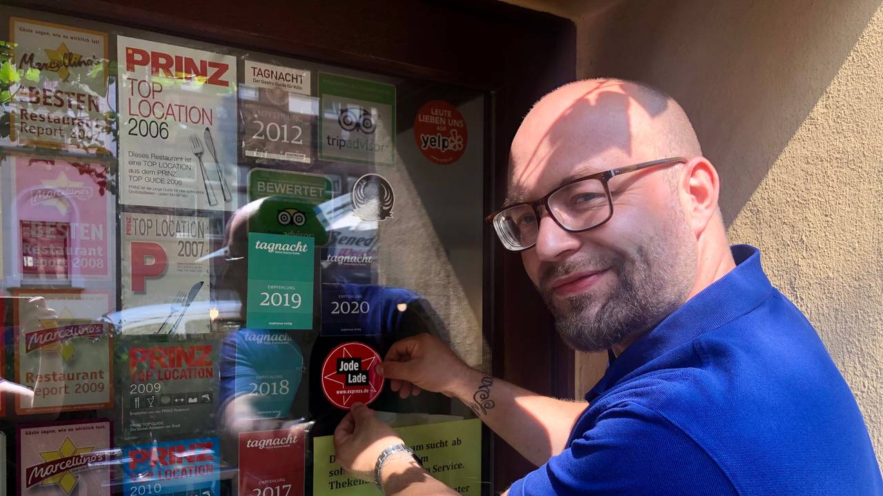 Geschäftsführer Janis Ruhbach klebt den „Jode Lade“-Sticker an die Eingangstür des „Caminetto“.