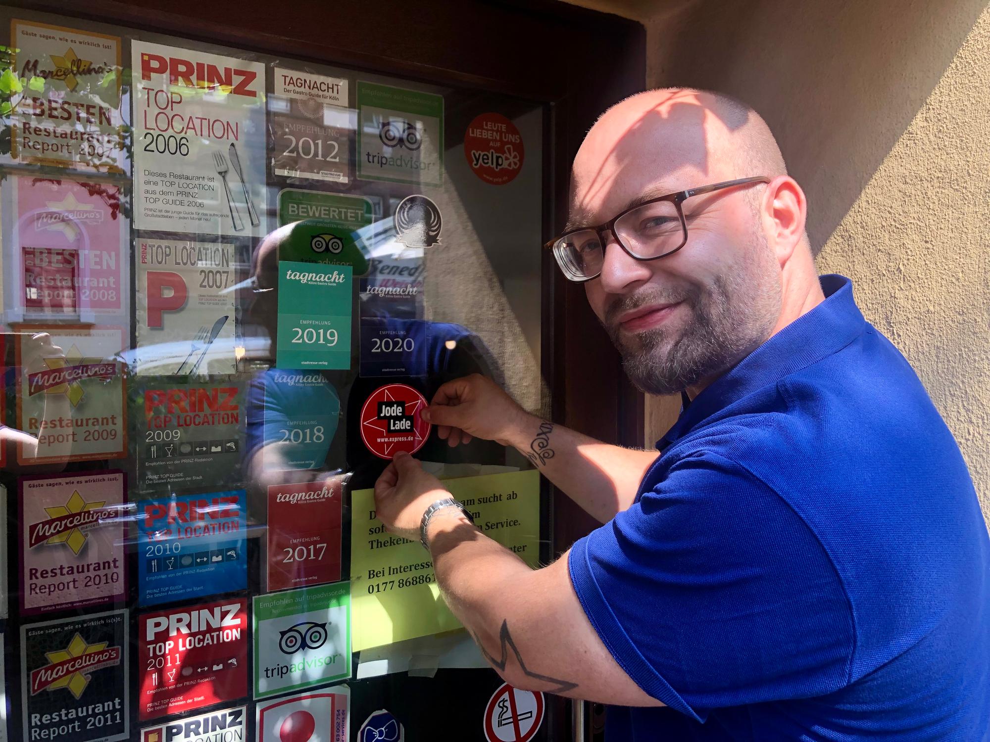Geschäftsführer Janis Ruhbach klebt den „Jode Lade“-Sticker an die Eingangstür des „Caminetto“.