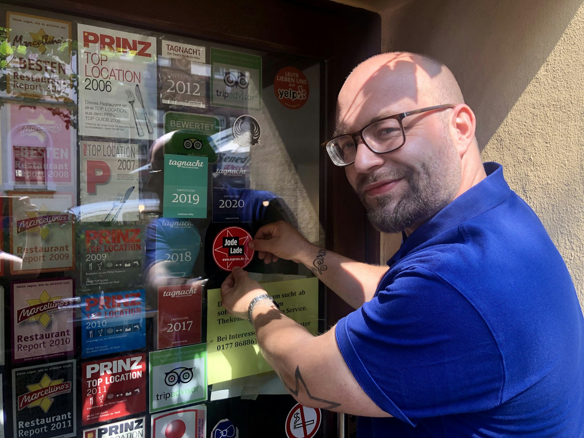 Geschäftsführer Janis Ruhbach klebt den „Jode Lade“-Sticker an die Eingangstür des „Caminetto“.