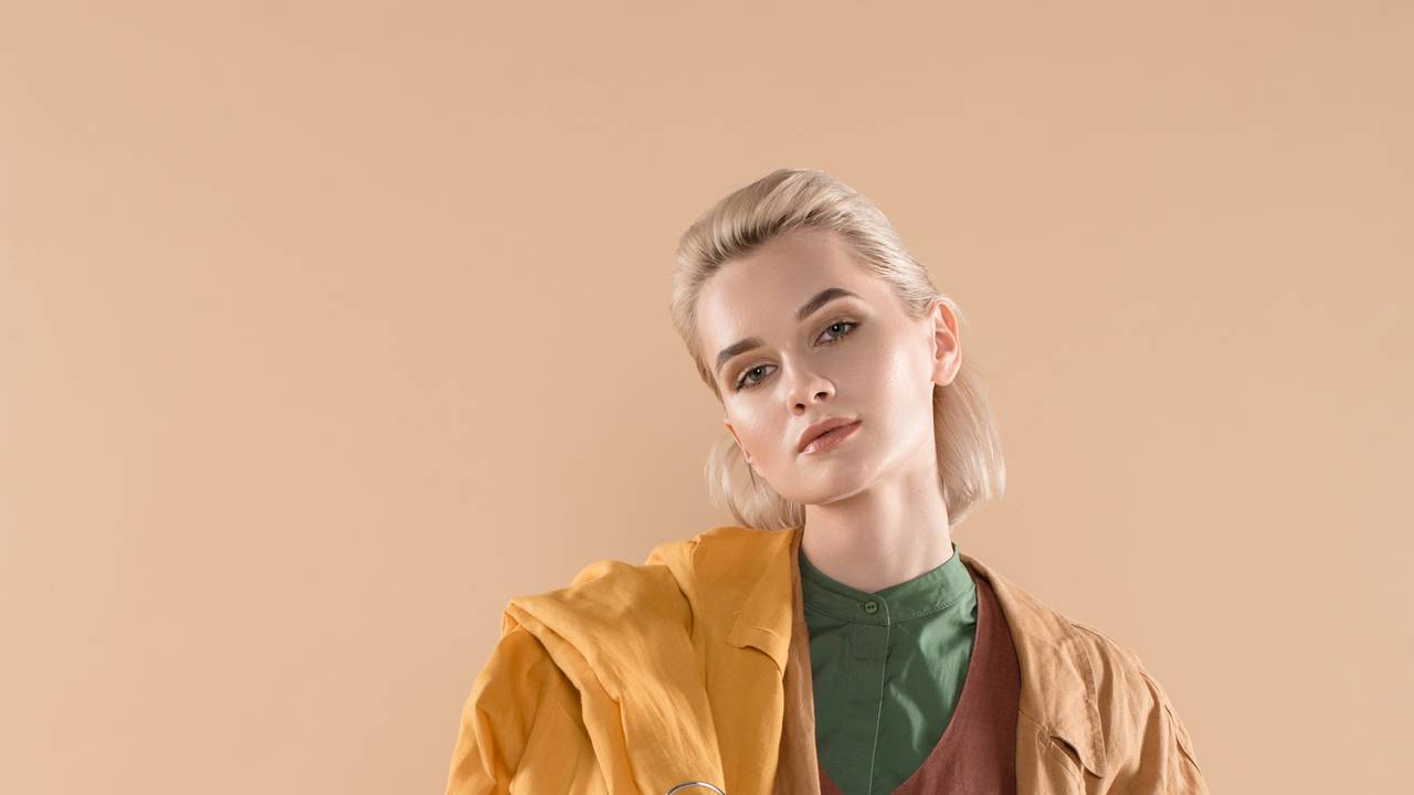 Eine junge blonde Frau hält einige Kleidungsstücke in der Hand.